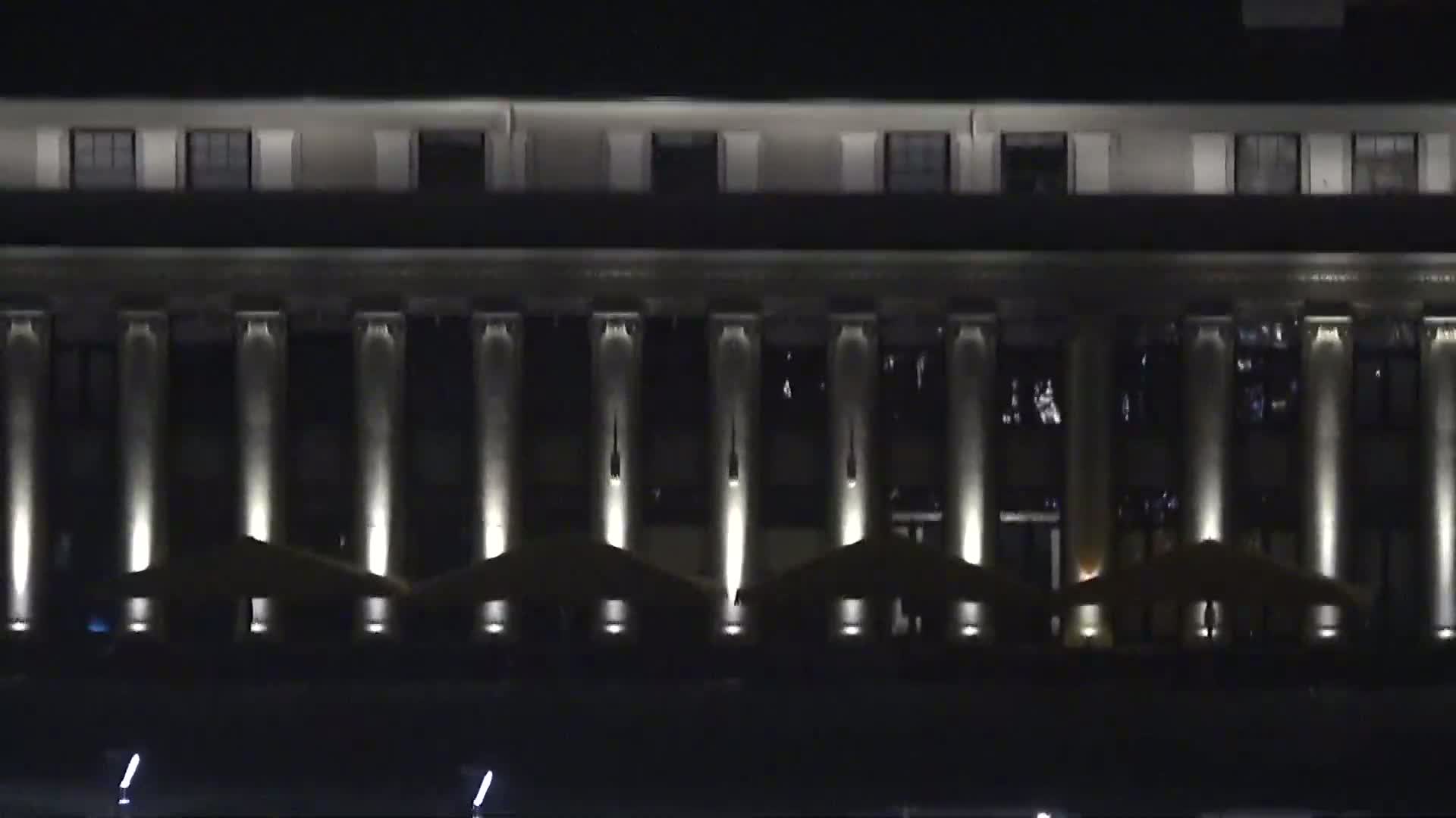 A large, classical-style building with numerous columns is illuminated at night.