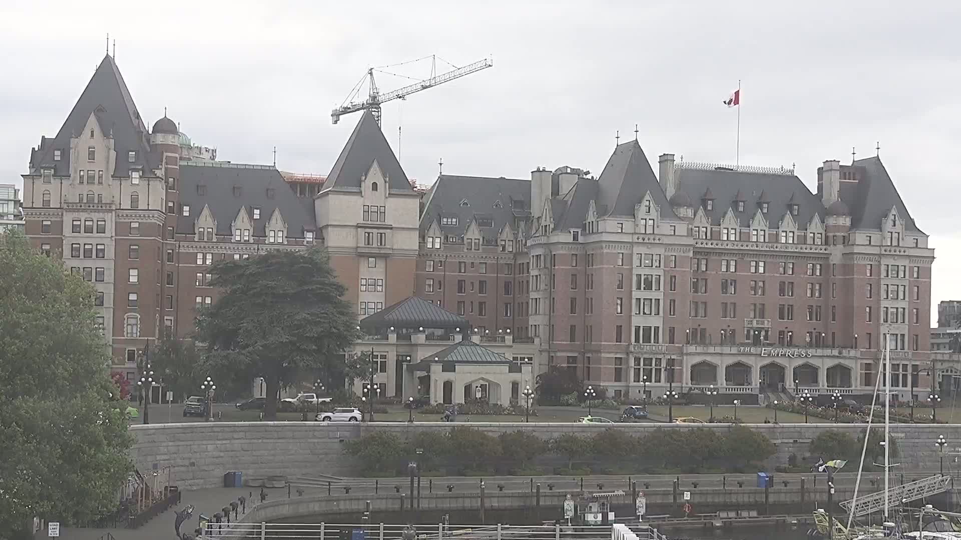 A large, ornate brick hotel stands on a waterfront, under an overcast sky, with a construction crane visible in the background.