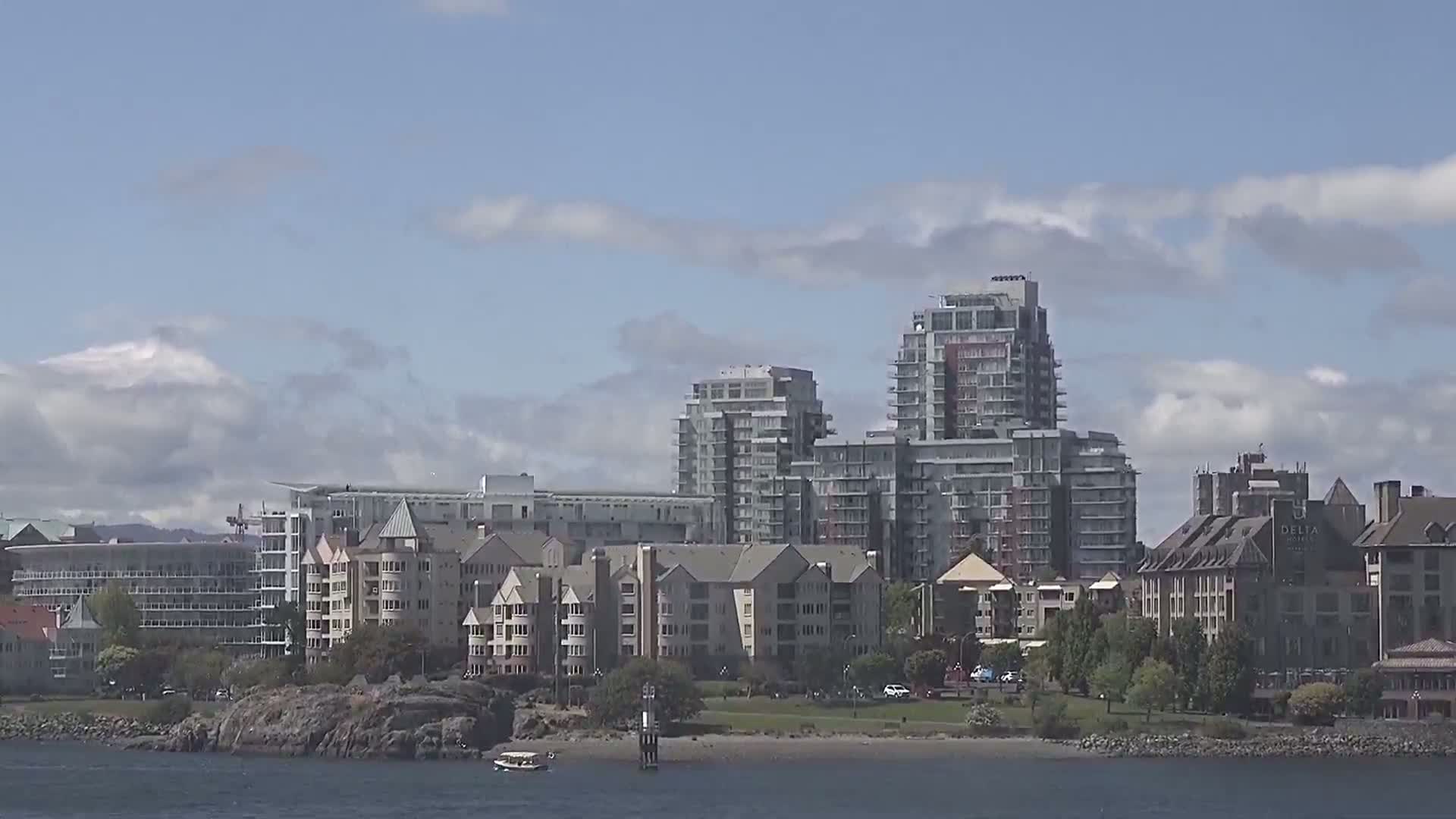 A waterfront city scene shows several apartment buildings and a hotel under a partly cloudy sky.