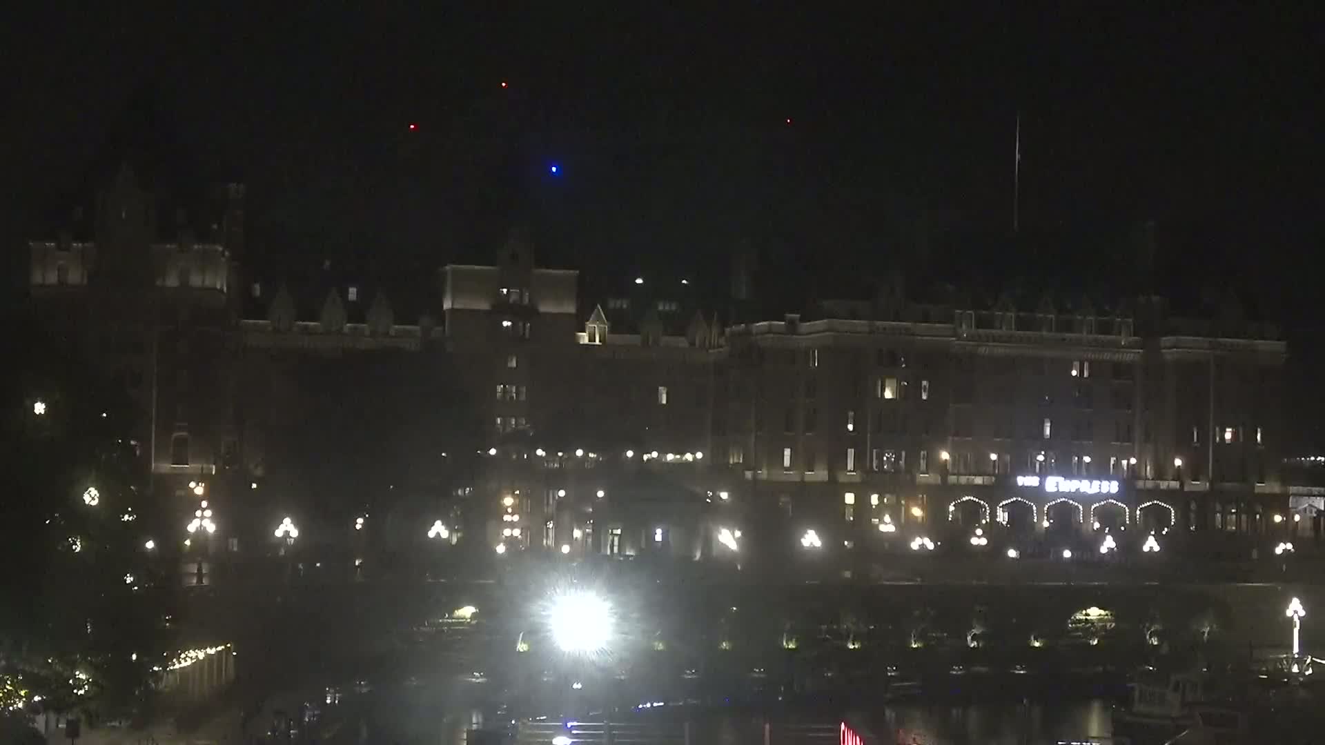 A large, dark building with lights illuminating its windows and exterior is visible at night, with several lights in the foreground and a few lights visible in the dark sky above.