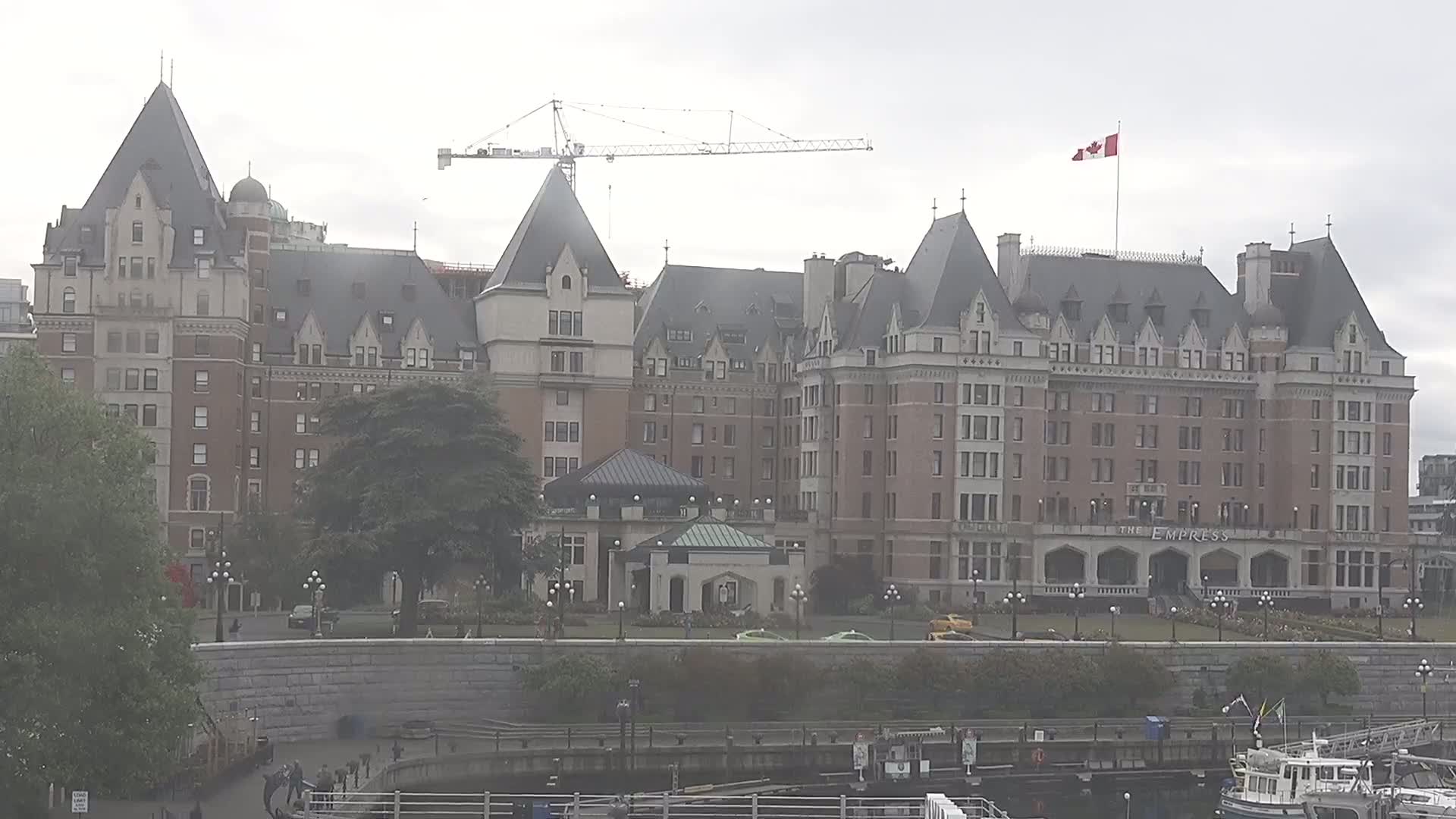 A large, castle-like hotel stands on a waterfront, partially obscured by trees and under an overcast sky.