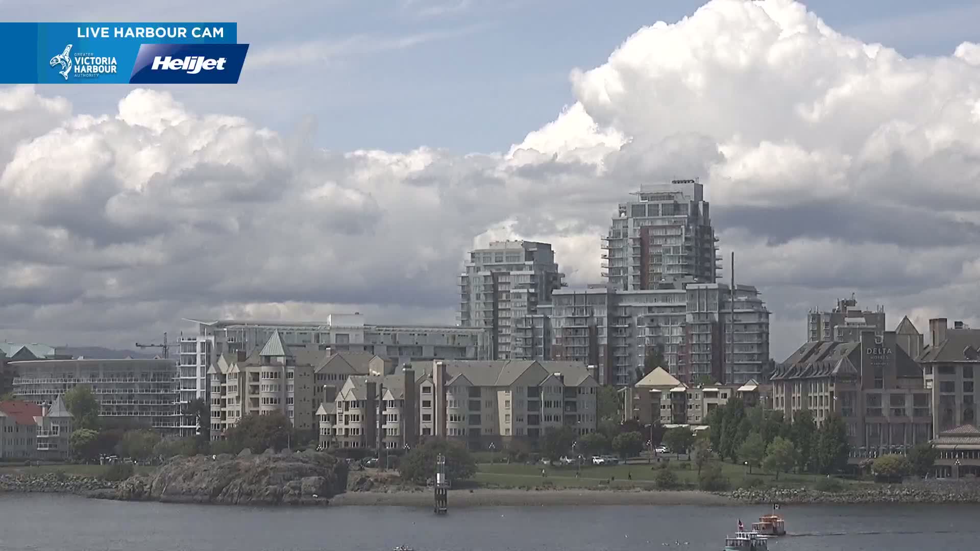 A waterfront scene shows several multi-story residential buildings and a hotel under a partly cloudy sky.