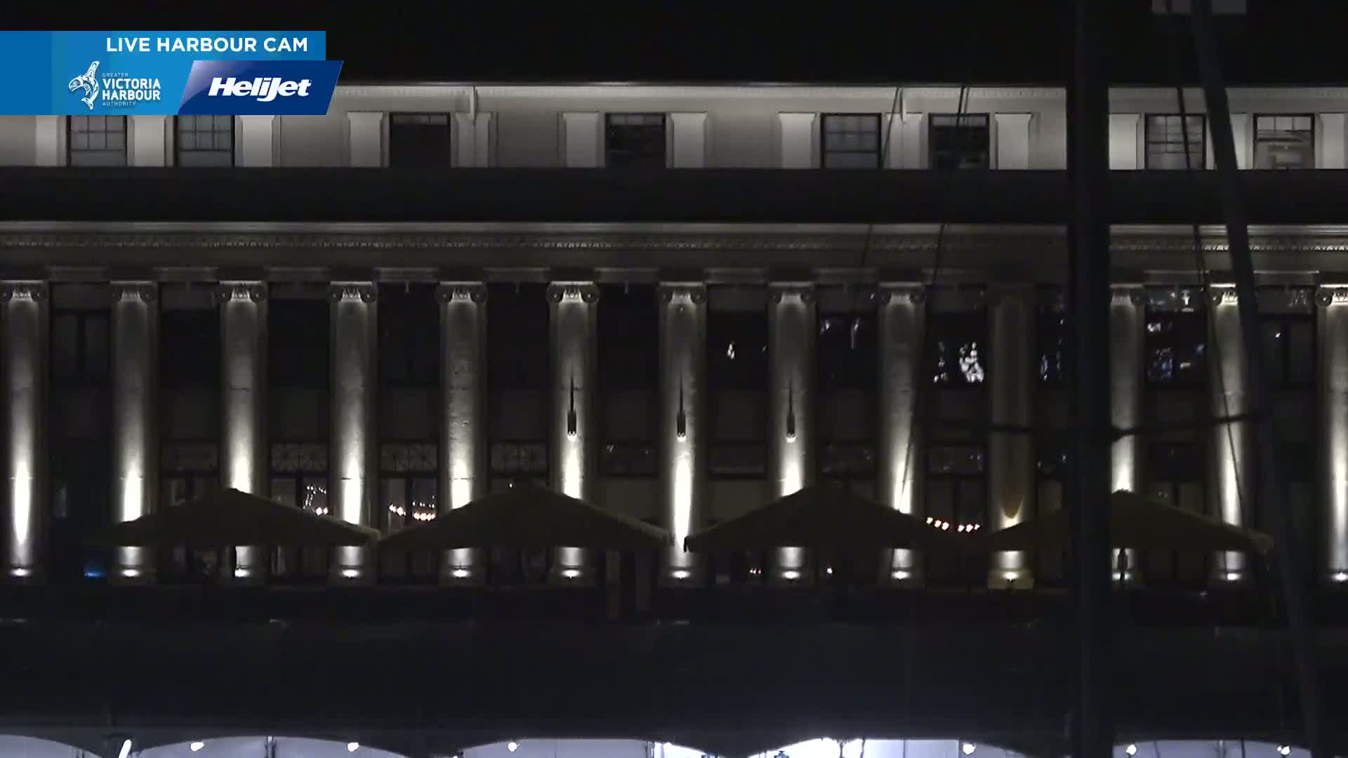 A large, multi-story building with columns is illuminated at night, and several outdoor patio umbrellas are set up in front of it.