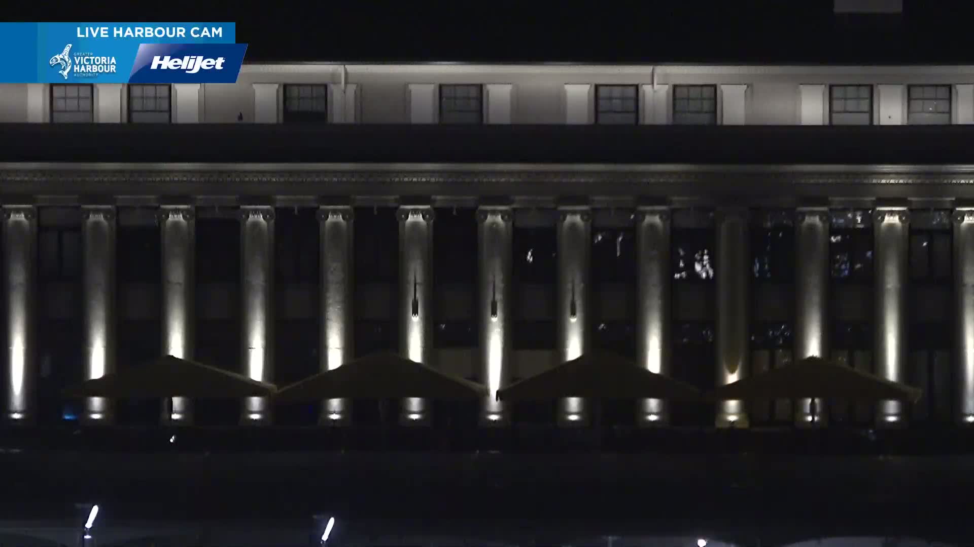 A large, dark building with many columns and outdoor patio umbrellas is illuminated at night.