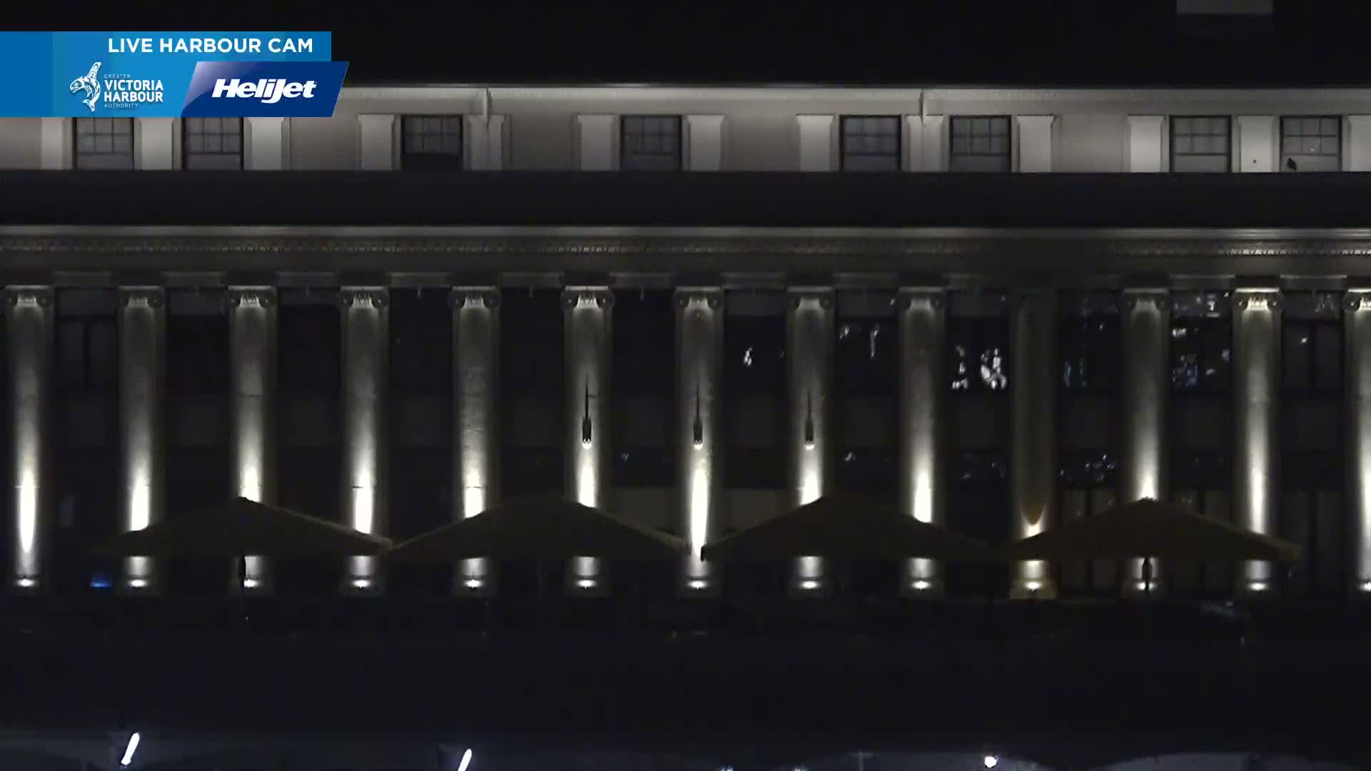 A large, classical-style building with illuminated columns and several outdoor umbrellas is shown at night.