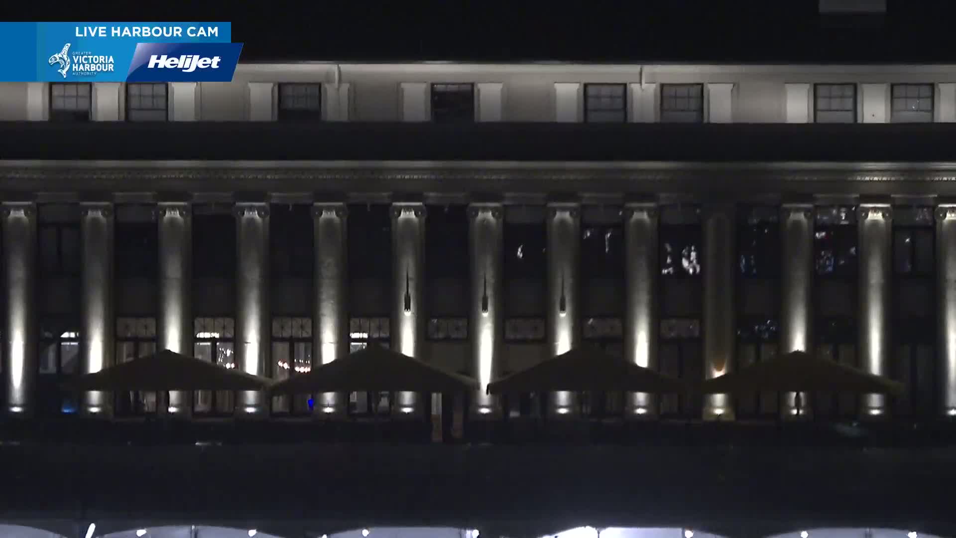 A large, multi-story building with columns is illuminated at night, with several outdoor patio umbrellas set up in front.