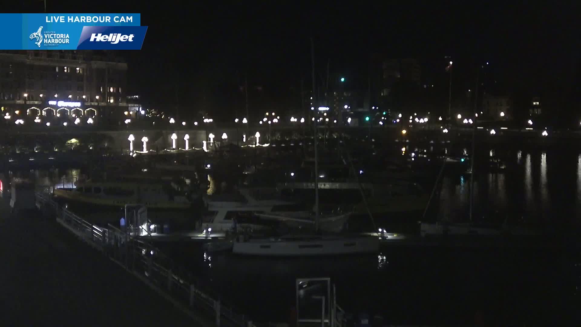 A nighttime view of a harbor filled with boats and illuminated by lights from buildings and docks on a calm night.