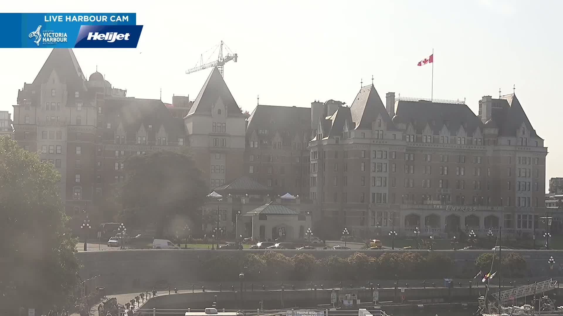 A large, historic hotel with a Canadian flag atop it is partially obscured by hazy sunlight.