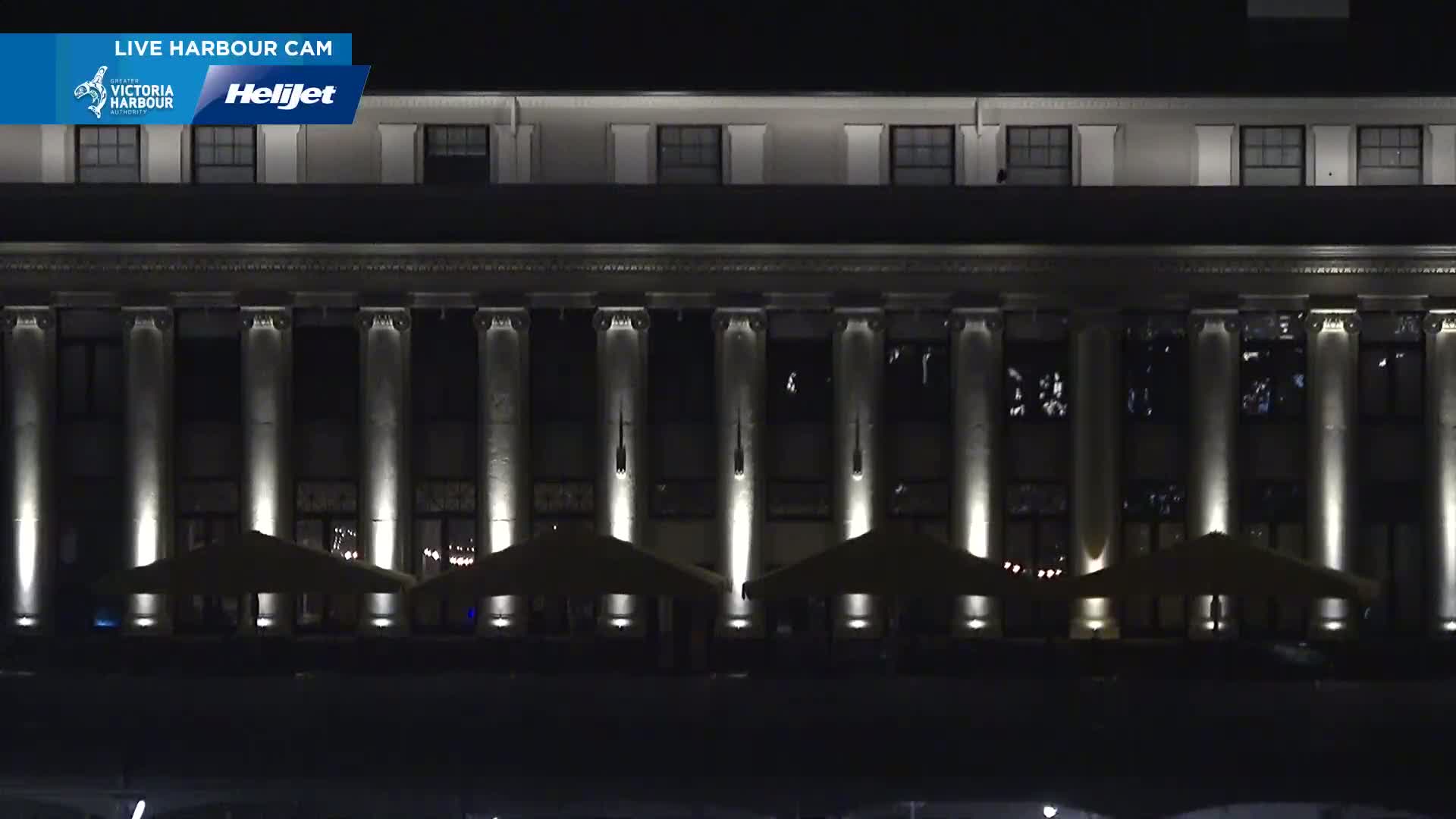 A large, classical-style building with columns is illuminated at night, with several outdoor umbrellas set up in front.