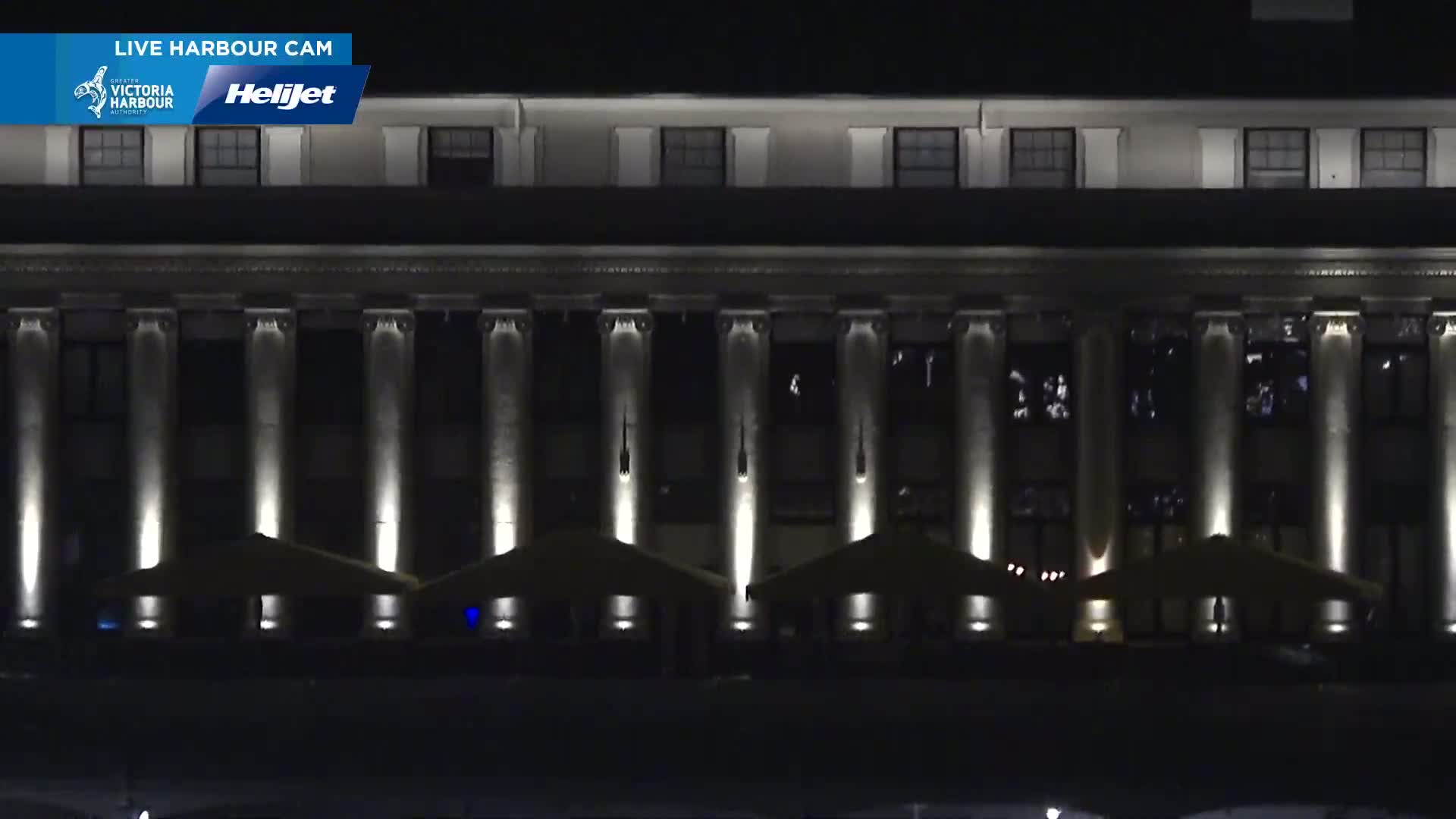 A large, dark building with many columns and outdoor patio umbrellas is illuminated at night.