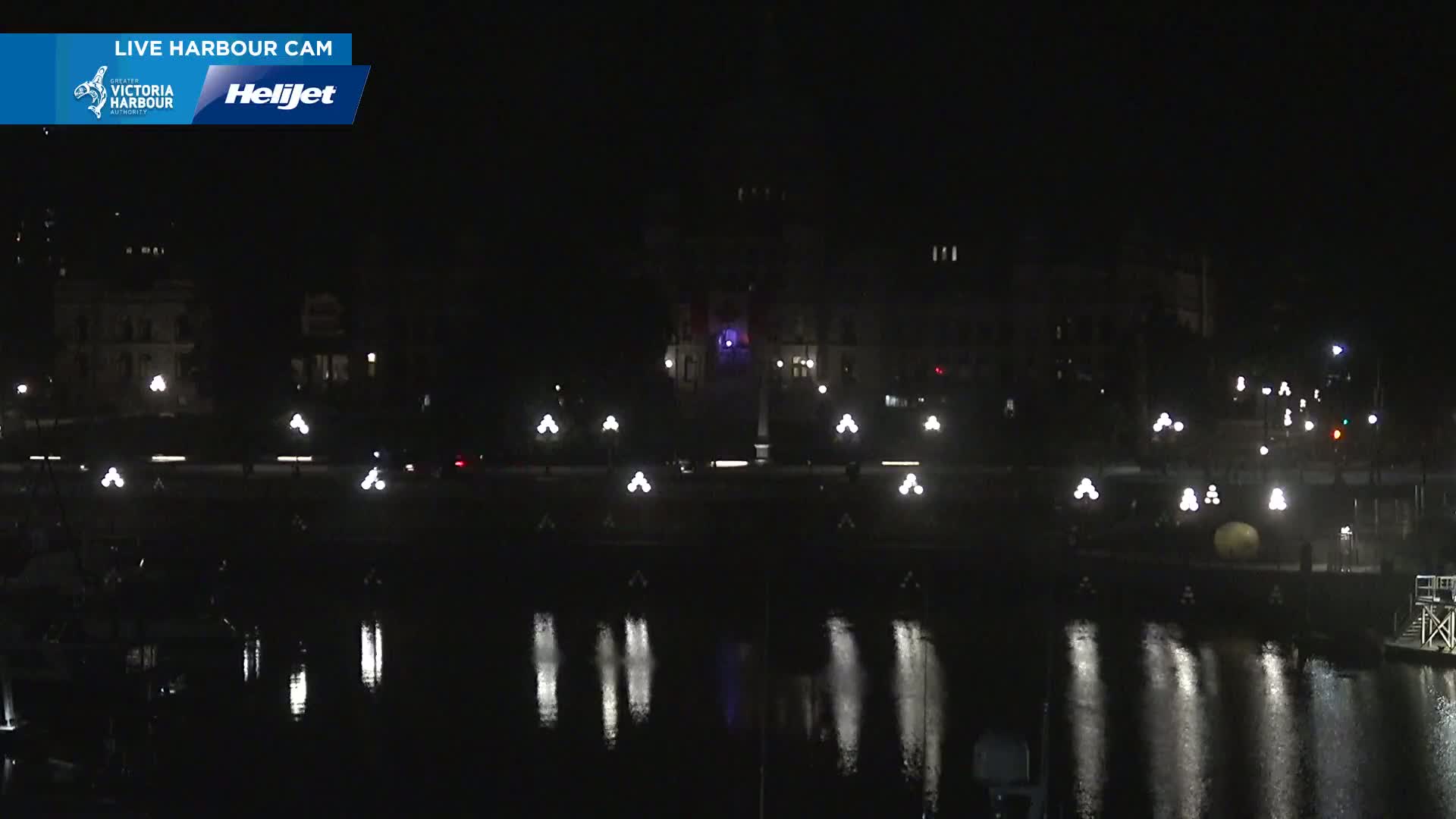 A nighttime view of a calm harbor reflecting the lights from buildings and streetlamps along a waterfront.