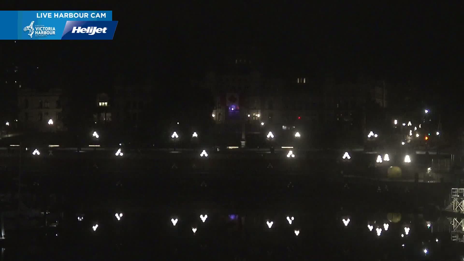 A nighttime view of a calm harbor reflecting the lights from buildings and streetlamps along a waterfront.