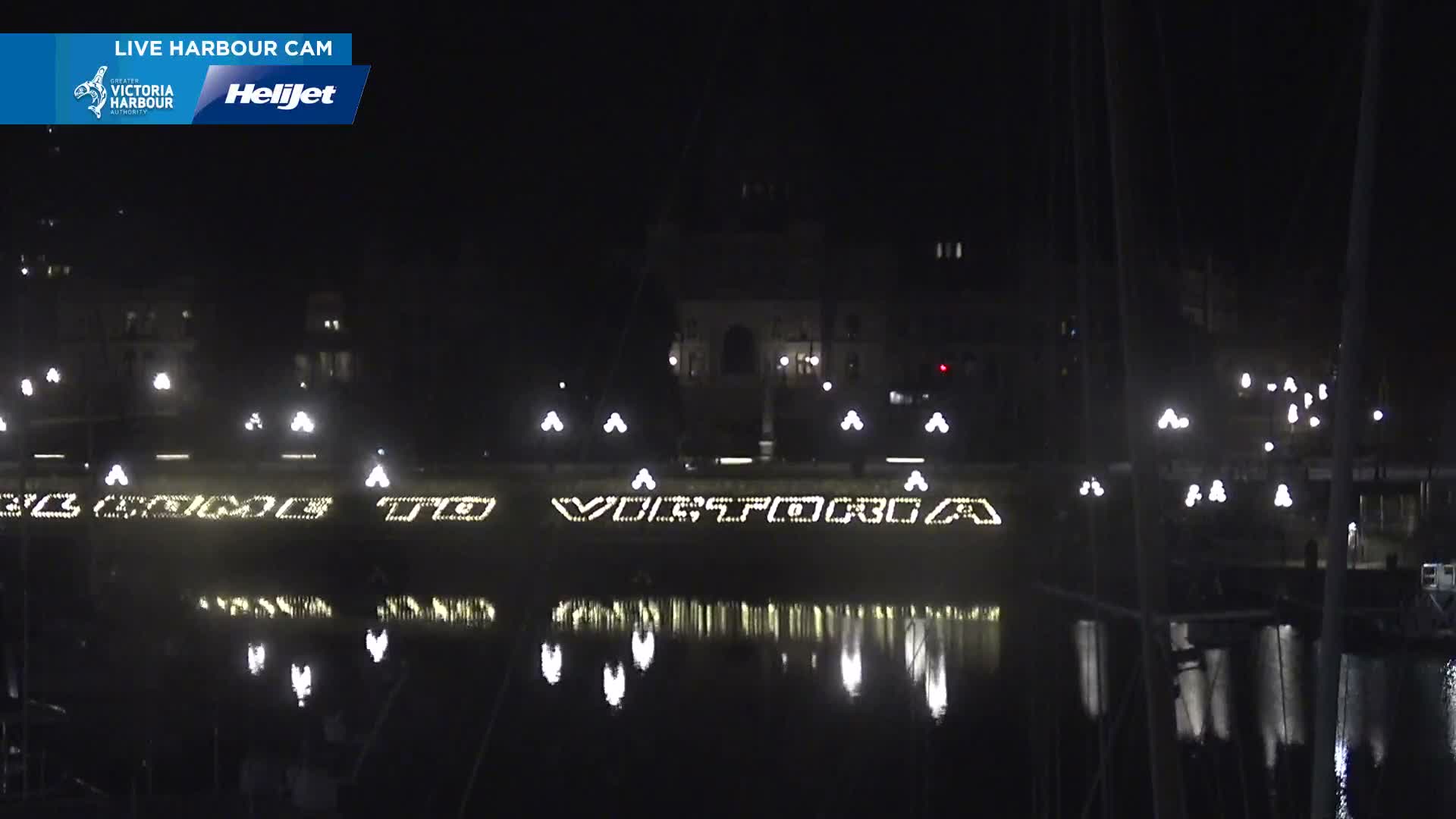 A nighttime view of a calm harbor reflecting the lights from buildings and streetlamps along a waterfront.