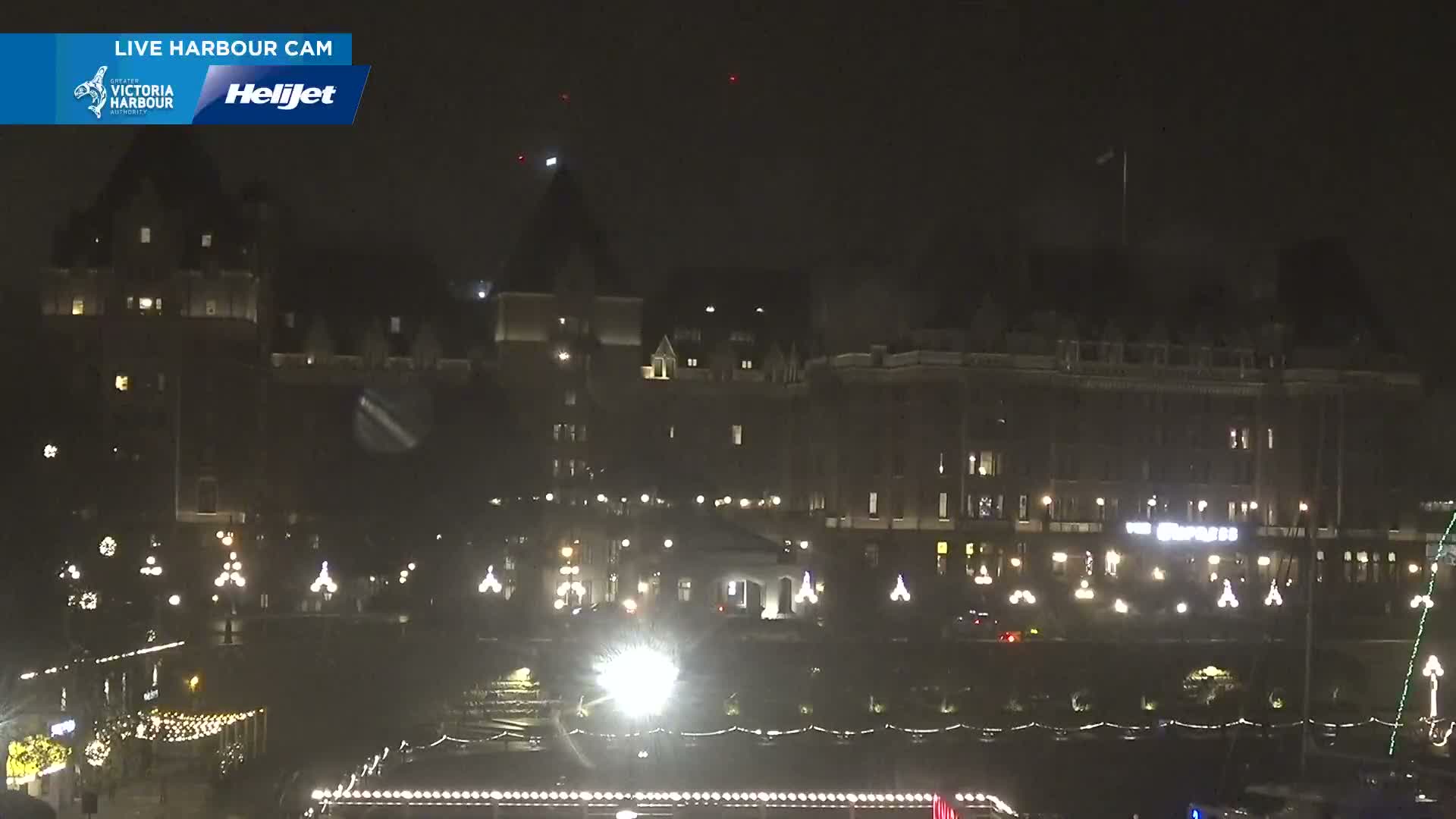 Grand buildings and festive string lights illuminate a hazy waterfront scene at night.