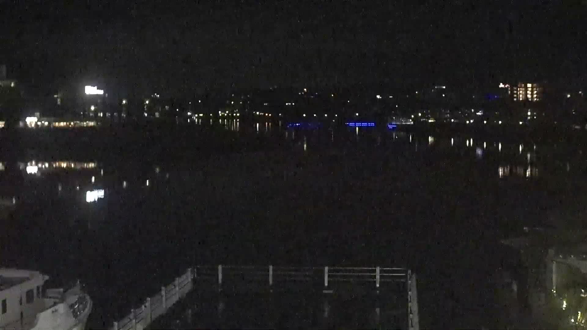The image displays a large, ornate building illuminated at night with many lights, overlooking a festive waterfront area adorned with numerous bright decorations, all under a clear sky.