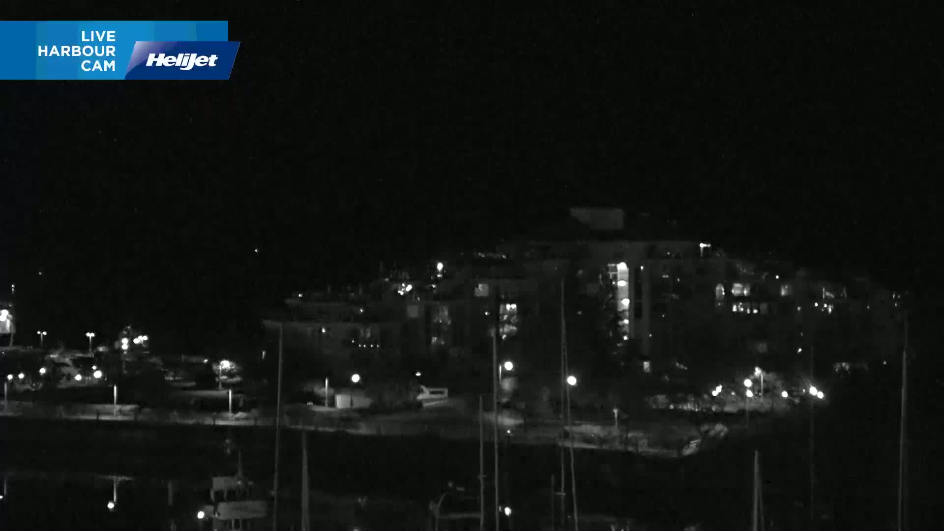 A nighttime view of a harbor with a multi-story building and boats, under a clear, dark sky.