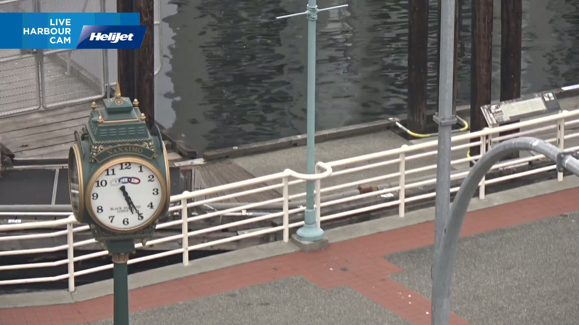 An ornate clock stands near a railing overlooking calm, dark water.