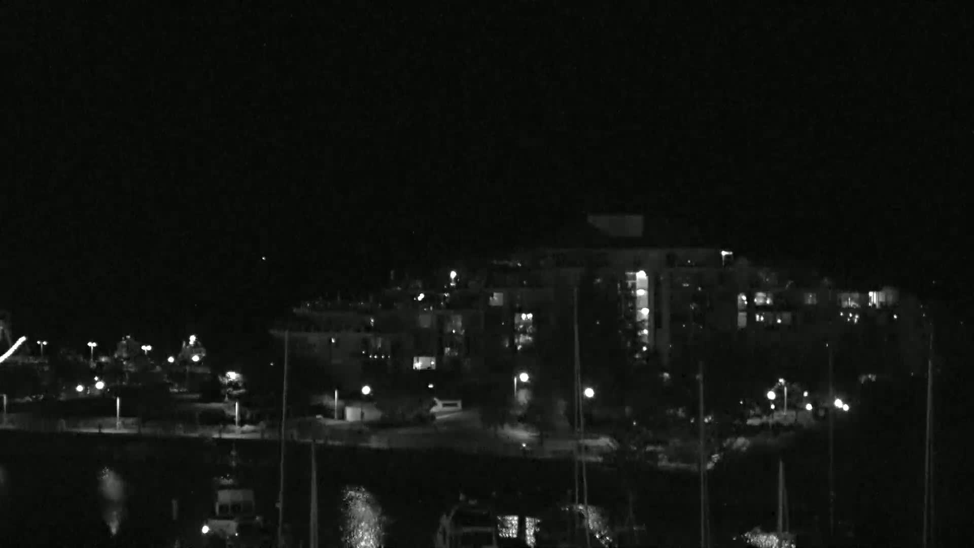 A nighttime view of a waterfront area with a multi-story building and boats docked, under a dark, clear sky.