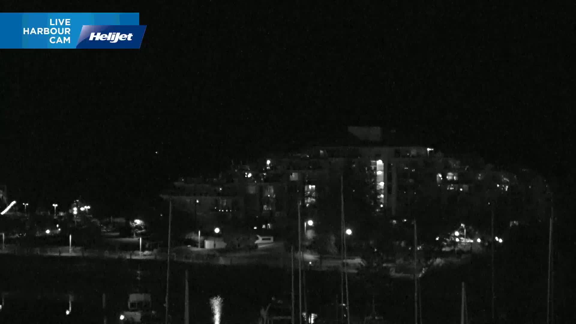 A nighttime, low-light view of a harbor with boats and a multi-story building illuminated by scattered lights.
