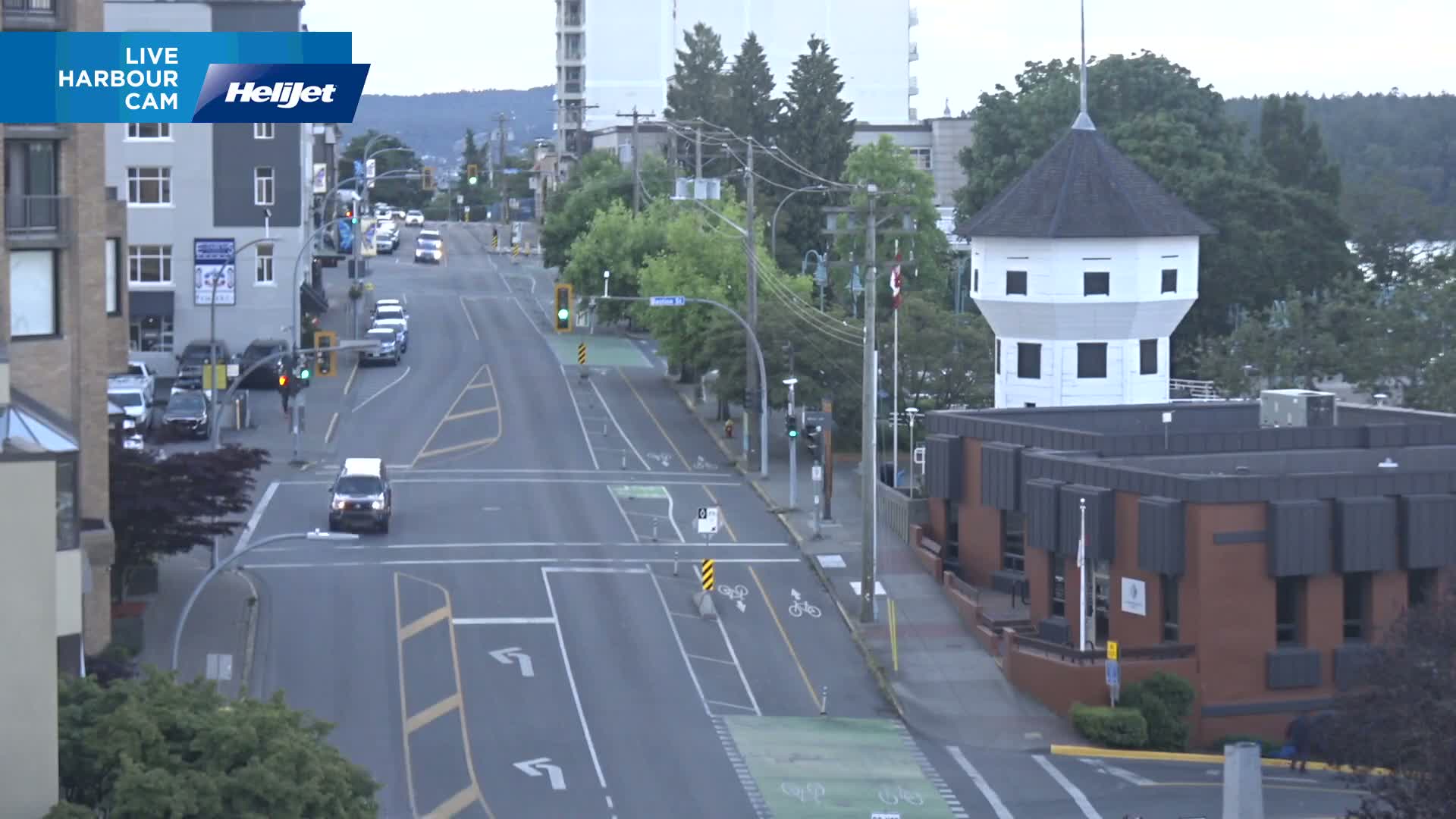 A mostly empty city street on an overcast day, with a white octagonal tower and a brick building visible in the foreground.