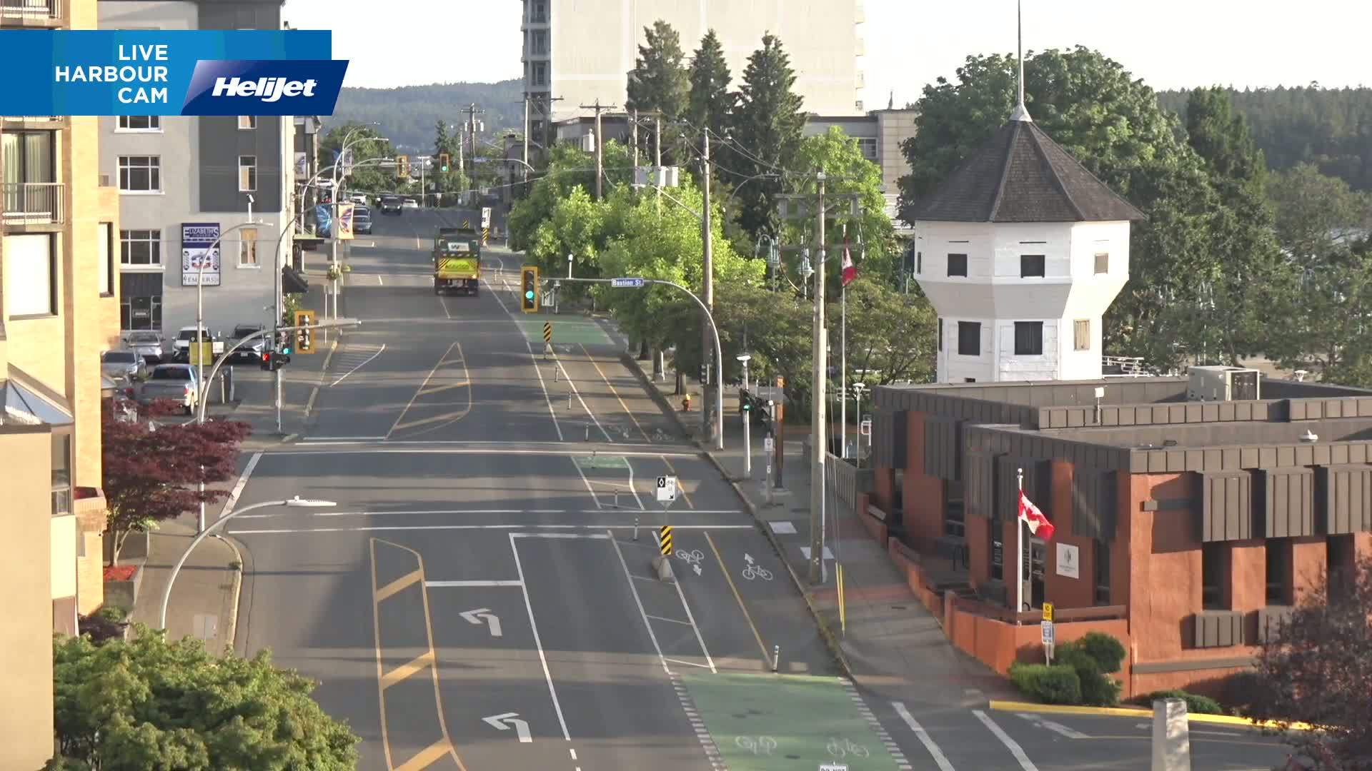 A sunny day shows a city street with bike lanes, a traffic intersection, and a white octagonal tower next to a low brick building.