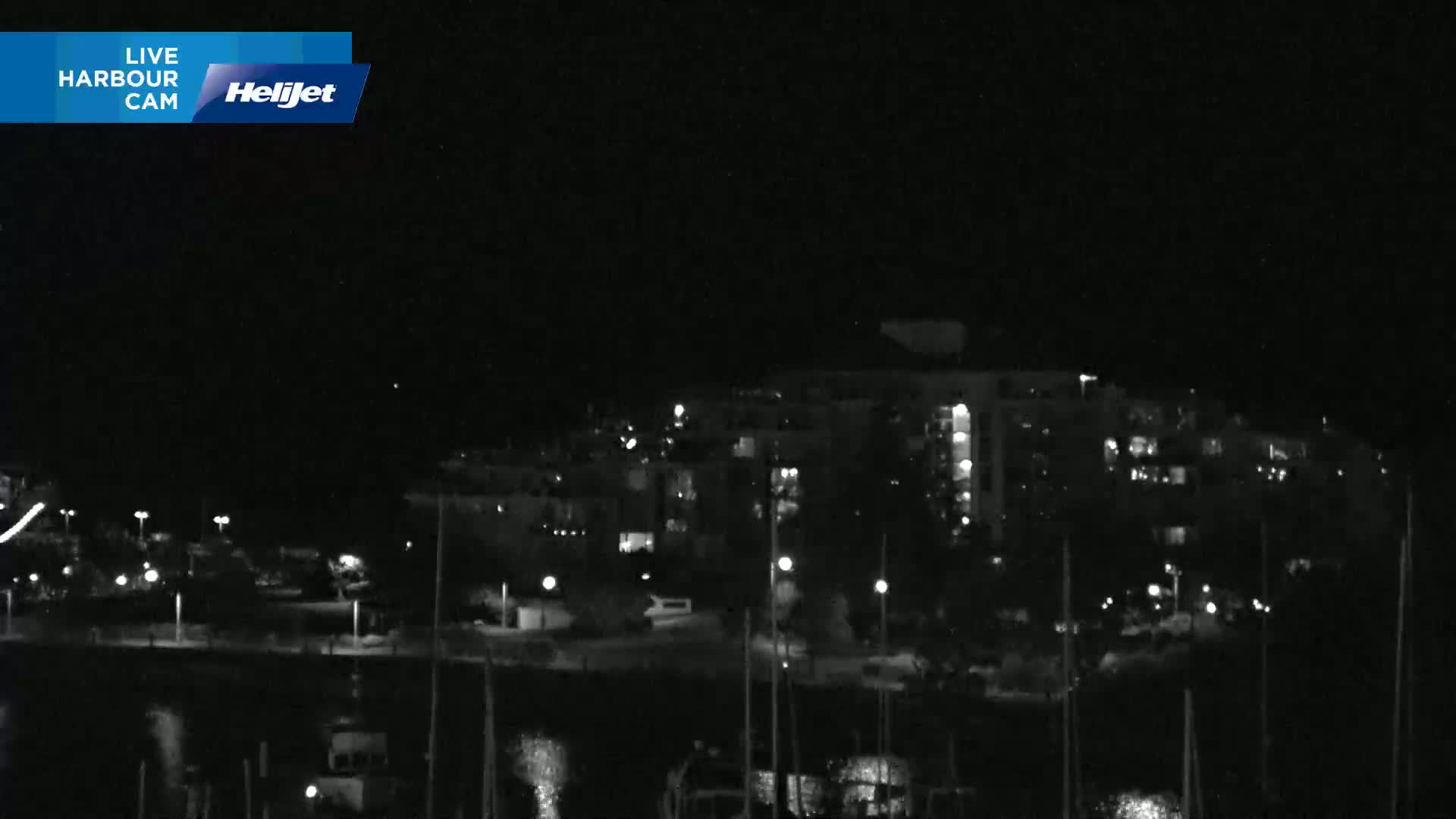 A nighttime, low-light view of a harbor with boats and a multi-story building in the background.
