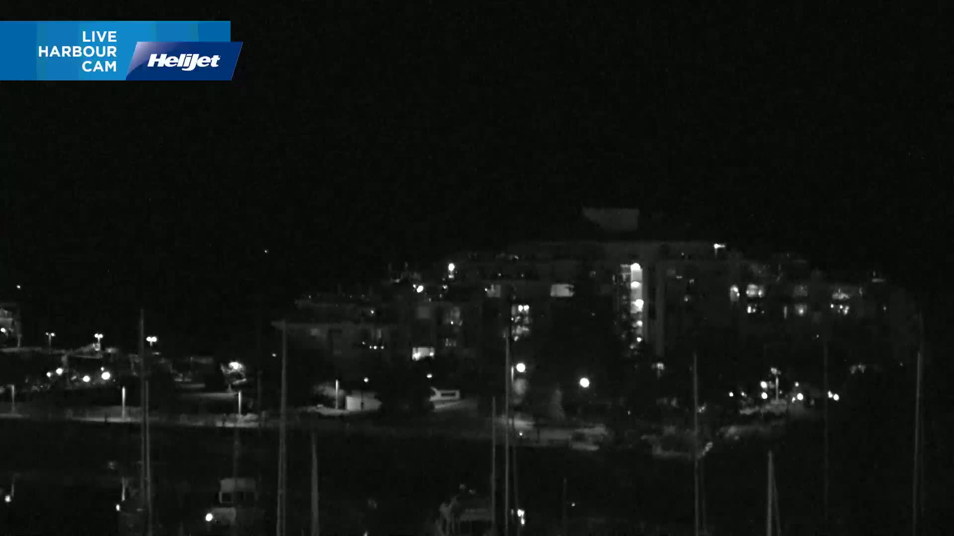 A nighttime, low-light view of a harbor with boats and a building complex illuminated by scattered lights.