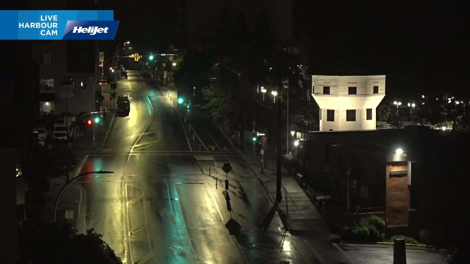 A nighttime, high-angle view shows a mostly empty street intersection with a white, octagonal tower and a building illuminated by streetlights.