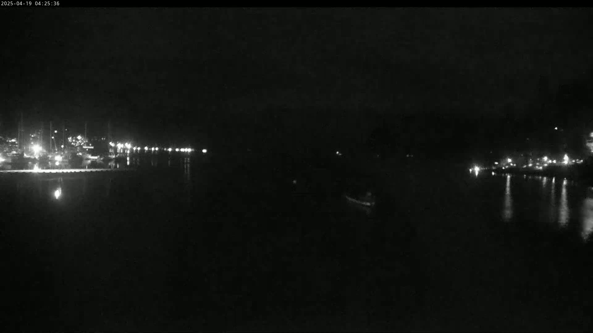 A nighttime view of a dark body of water reflecting lights from a distant shoreline.