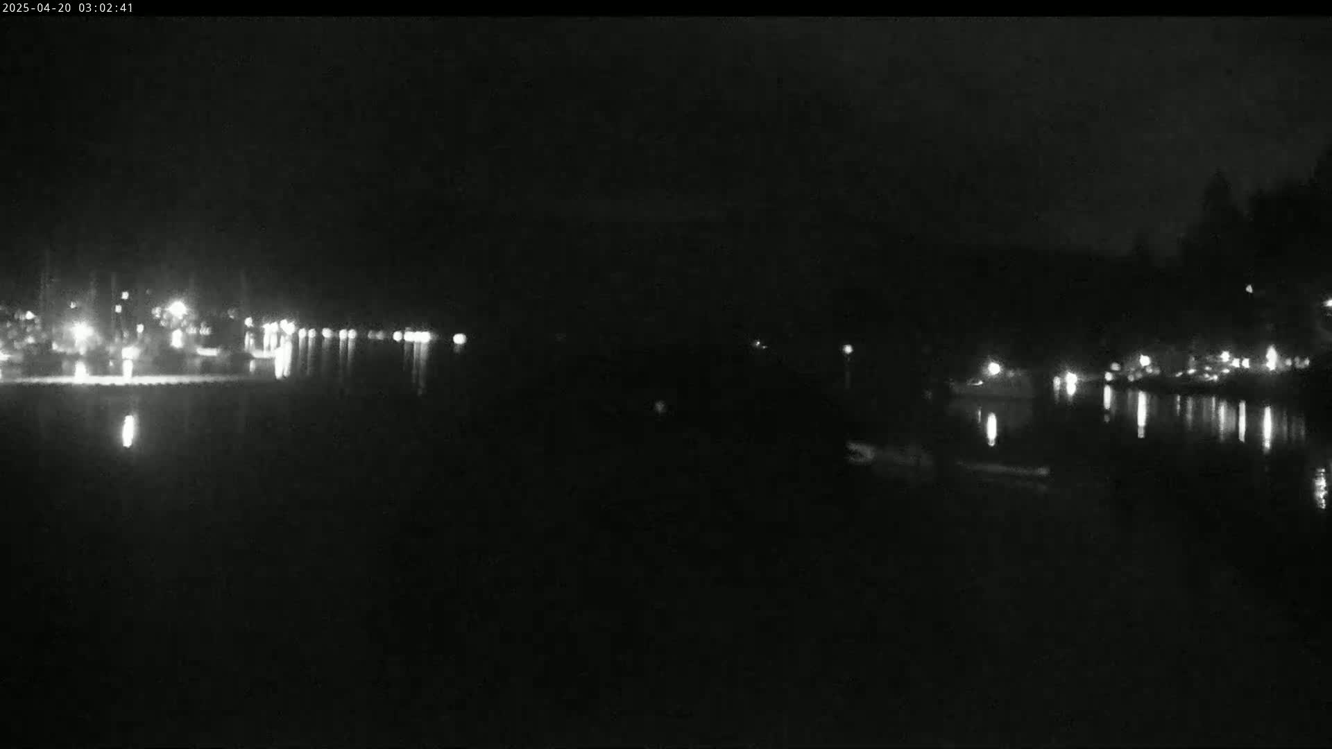 A nighttime view of a dark body of water reflecting lights from a shoreline at night.