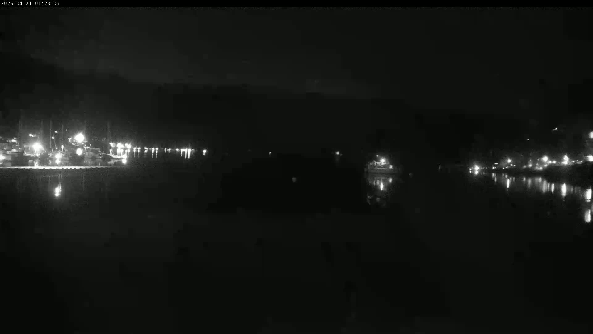 A dark nighttime view of a calm body of water reflecting the lights of a distant shoreline.