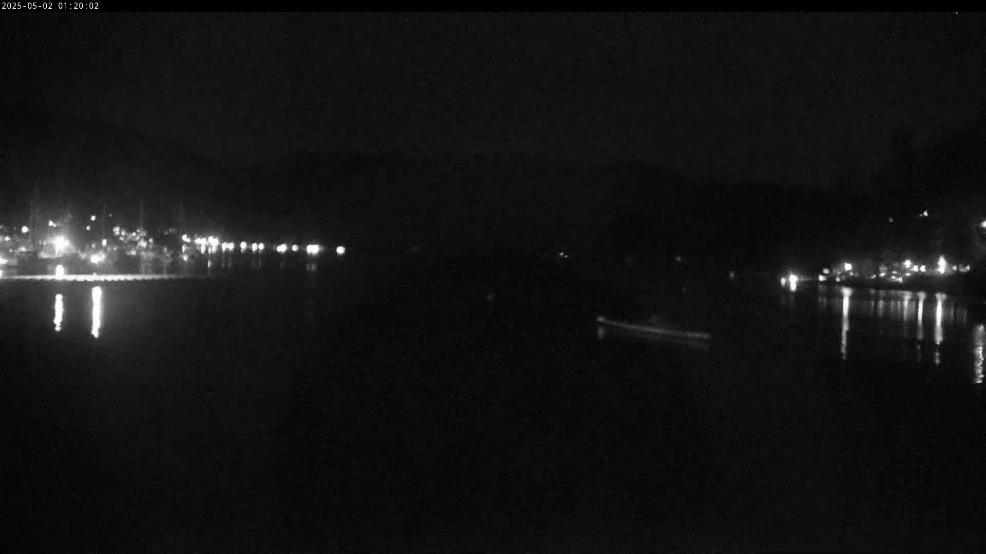 A dark, calm body of water reflects the lights of a distant town at night.