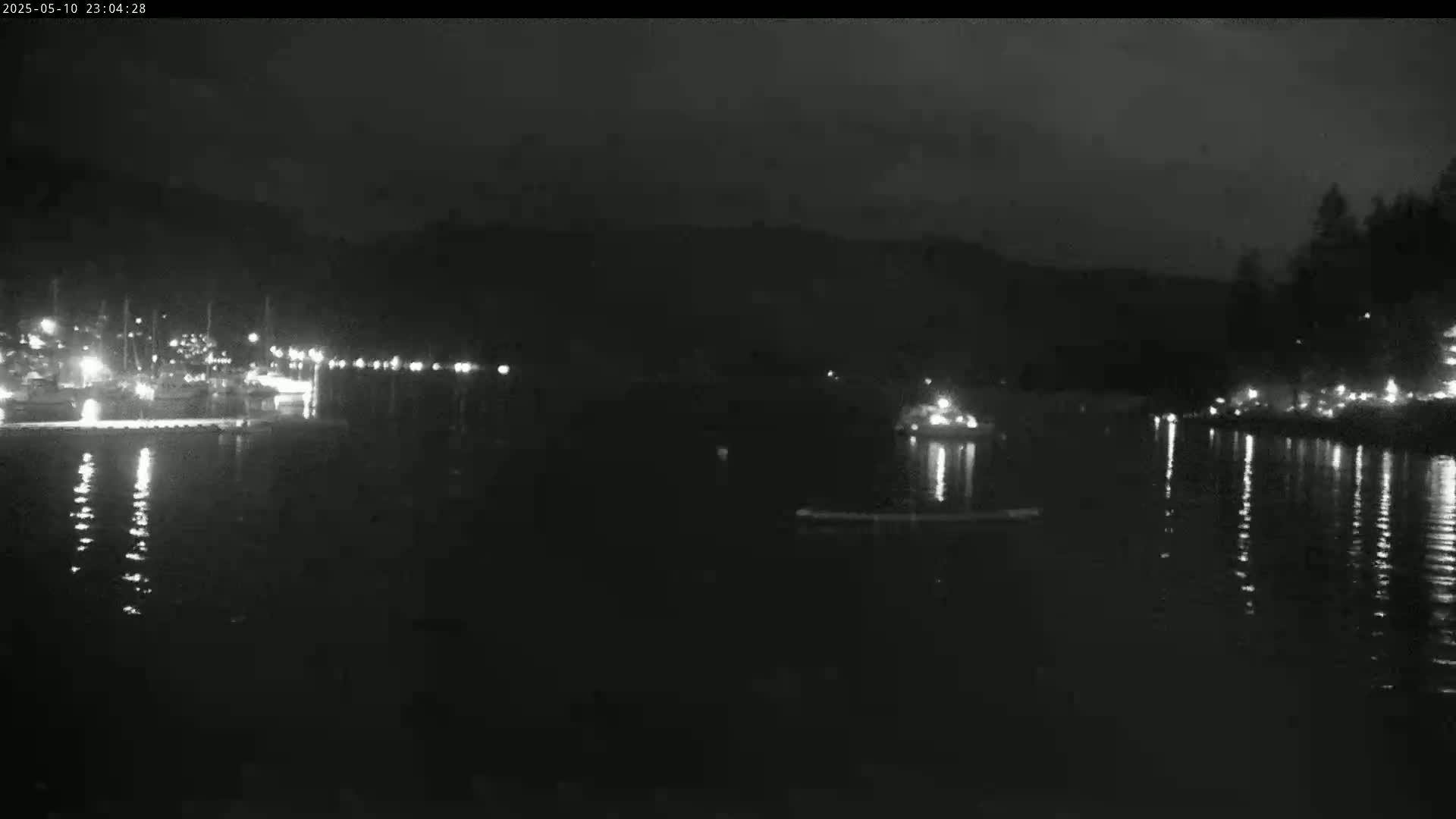 A nighttime view of a calm body of water reflecting lights from a distant shoreline with boats and buildings.