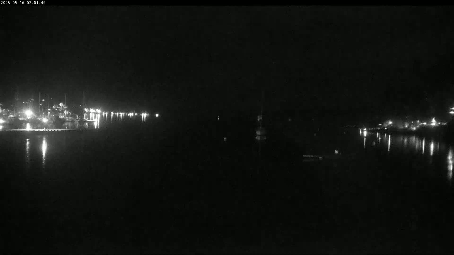 A nighttime view of a calm body of water reflecting the lights of a distant shoreline.