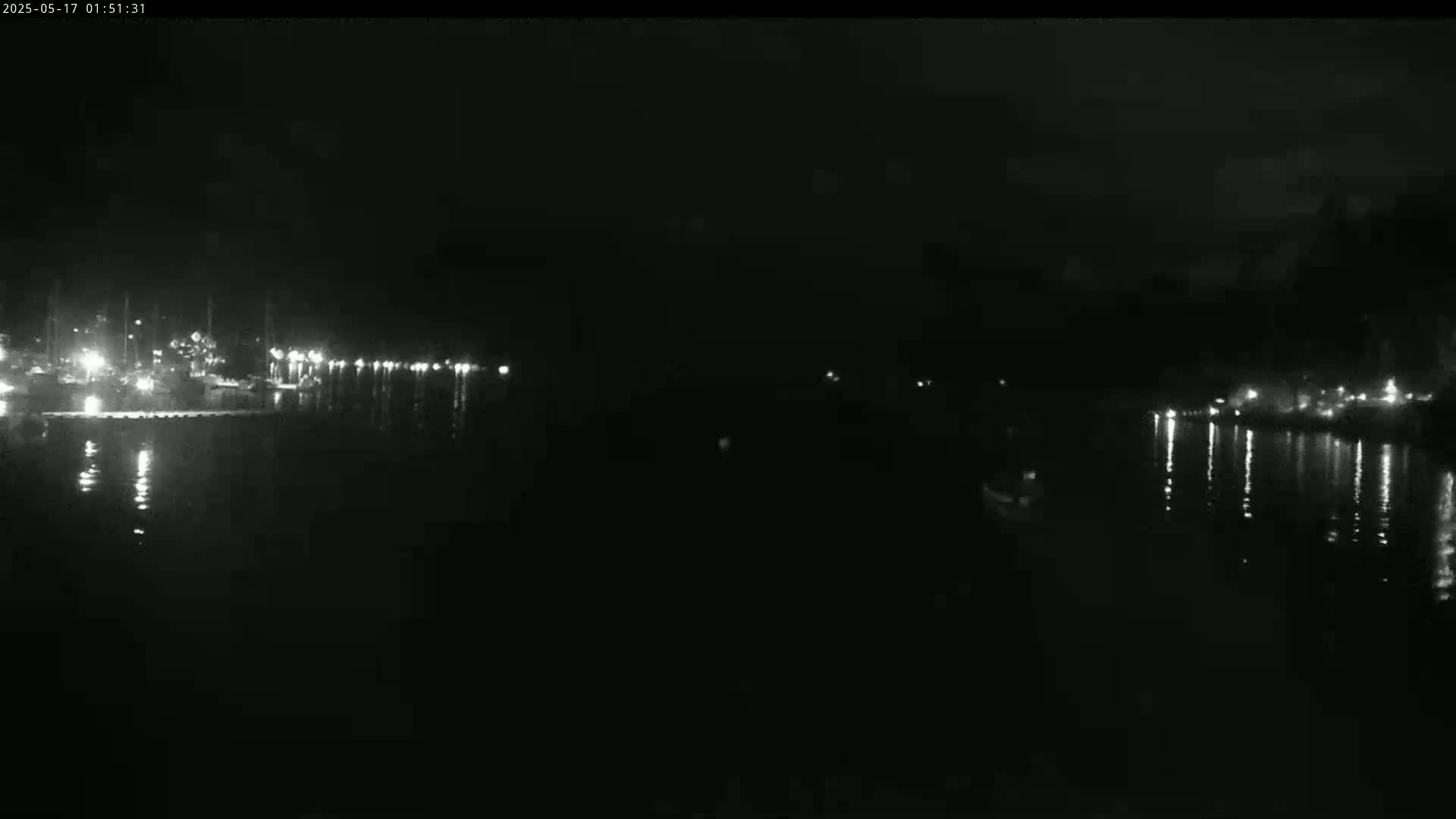 A nighttime, low-light view of a calm body of water reflecting the lights of a distant shoreline.