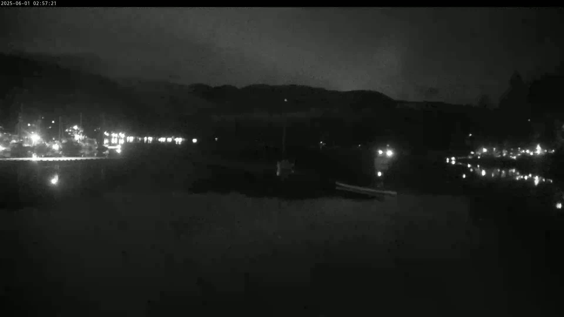 A nighttime view of a body of water with lights from buildings and vehicles visible along the shoreline under a dark sky.