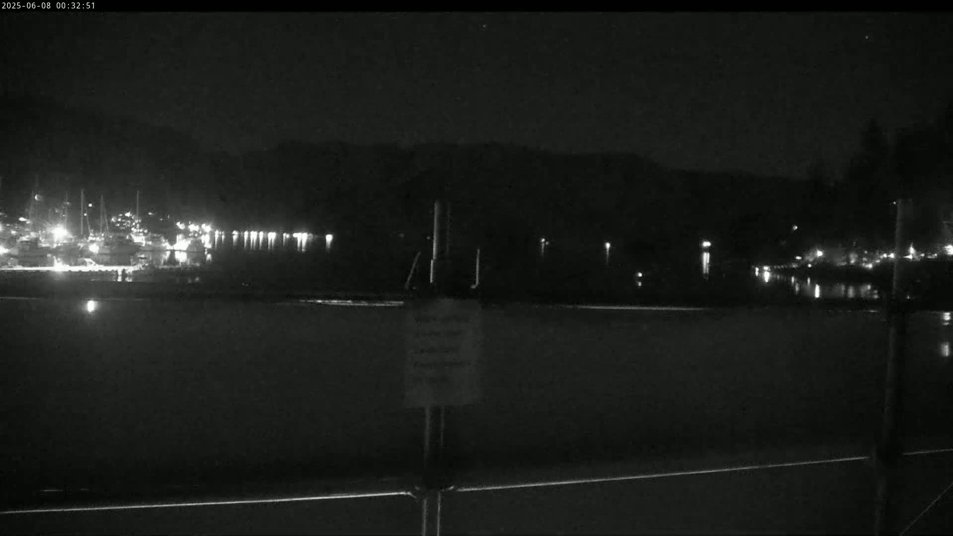 A nighttime view of a calm body of water with a marina in the background under a clear, dark sky.