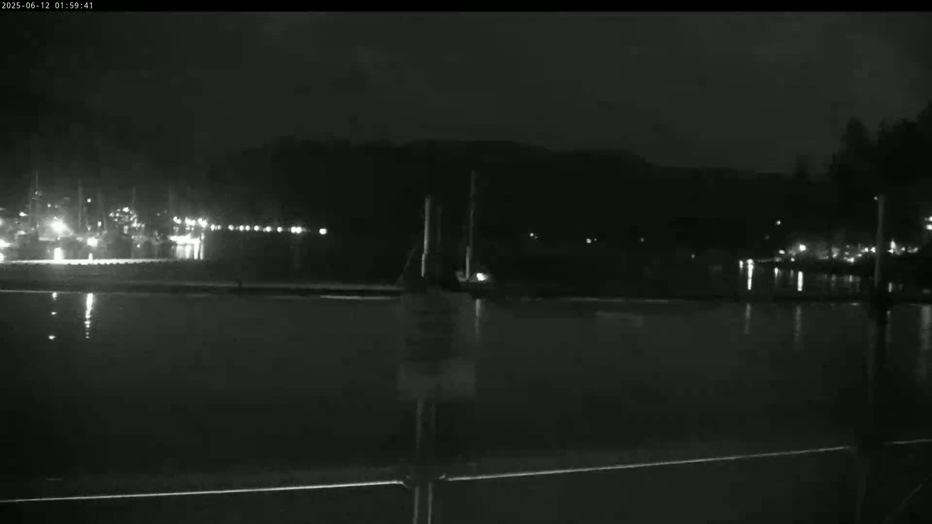 A nighttime, low-light view of a calm body of water reflecting the lights of a distant waterfront at night.