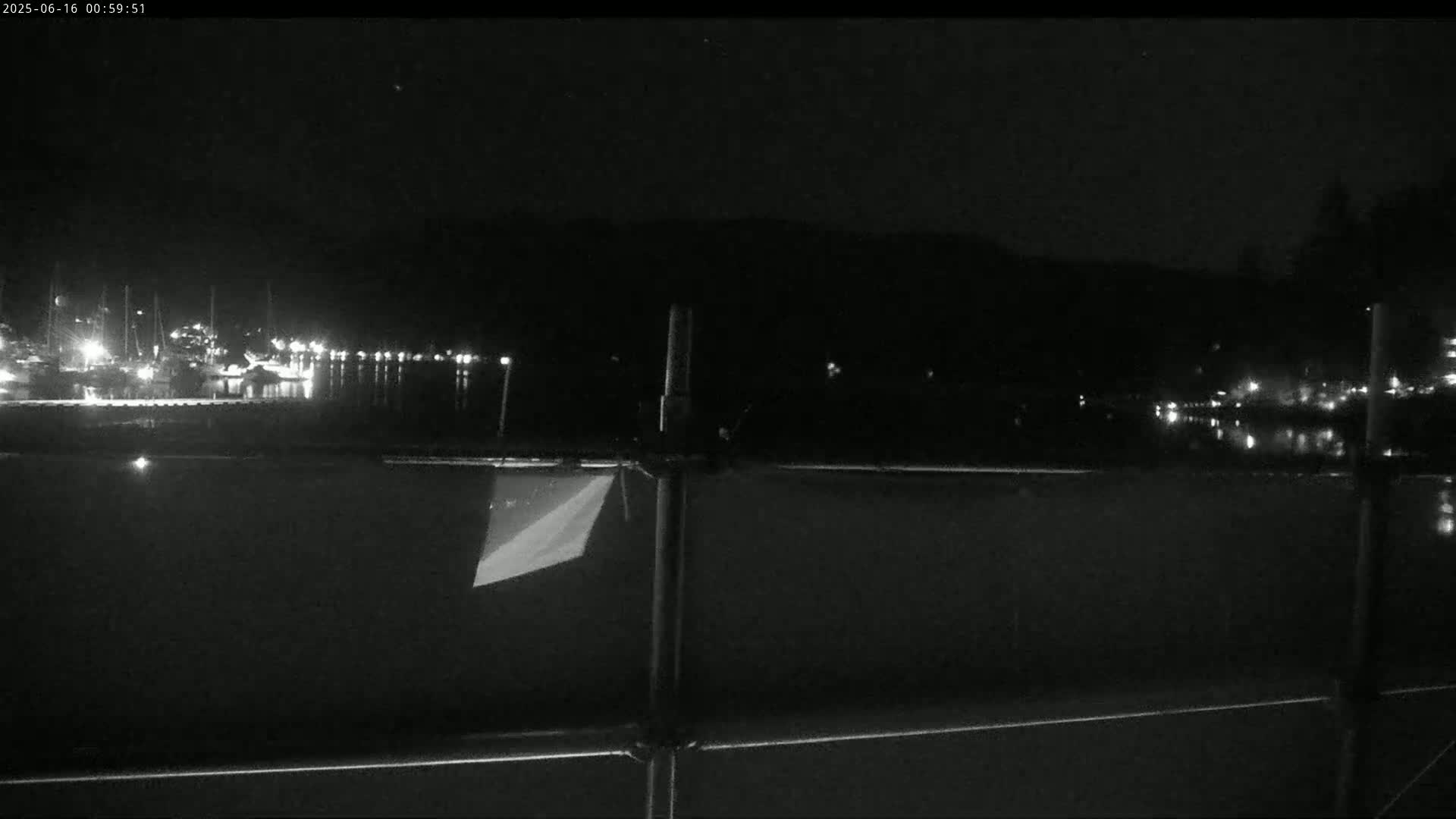 A nighttime view of a calm body of water with a marina in the distance, under a clear, dark sky.