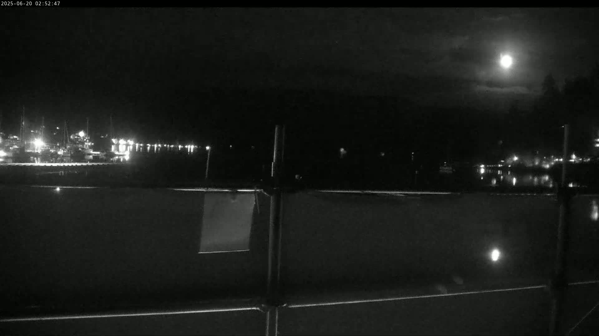 A nighttime view of a harbor with lights reflecting on the water under a bright moon.