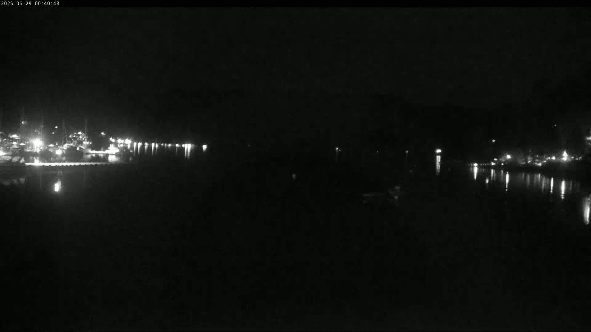 A nighttime view of a calm body of water with lights reflecting on its surface from a distant shoreline.
