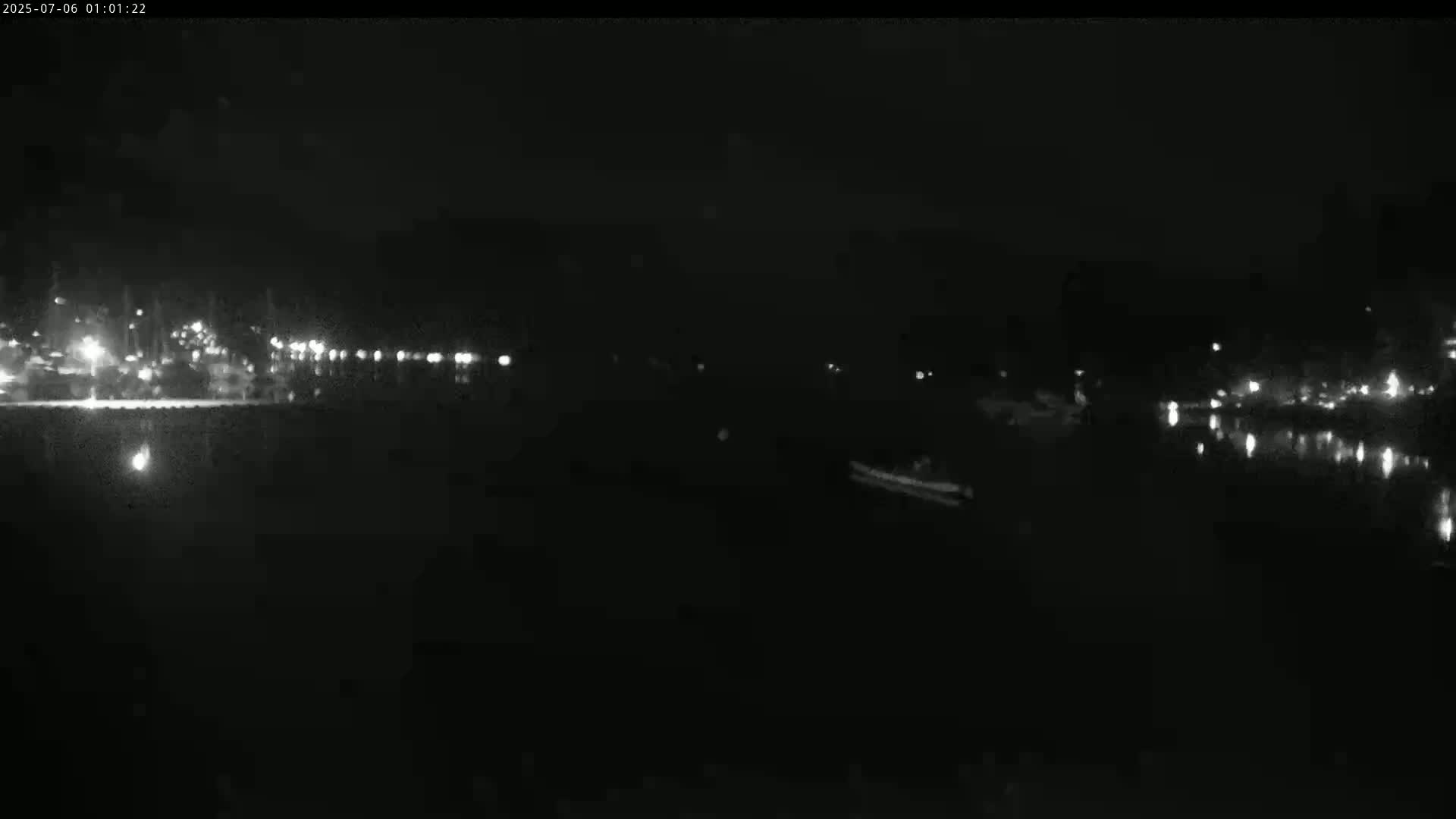A nighttime view of a dark body of water with a distant shoreline showing faint lights.