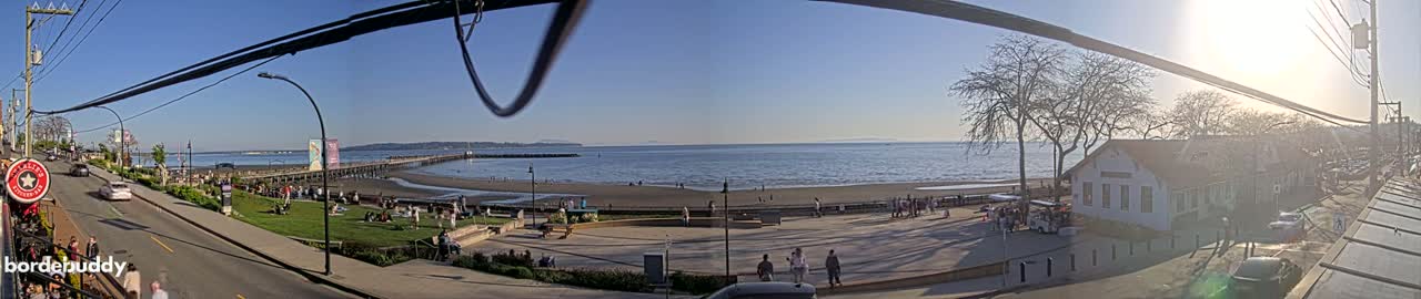 A sunny seaside town scene with a long pier, sandy beach, and people enjoying the outdoors.