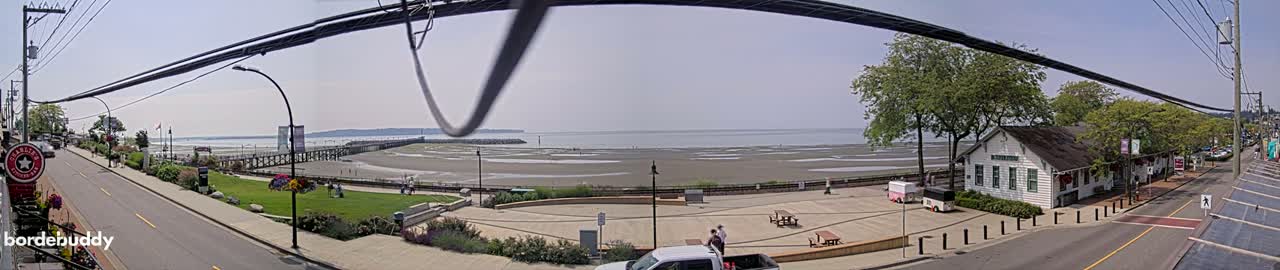 A seaside town on a sunny day with a wide sandy beach exposed at low tide, a long pier, and a white building near the shore.