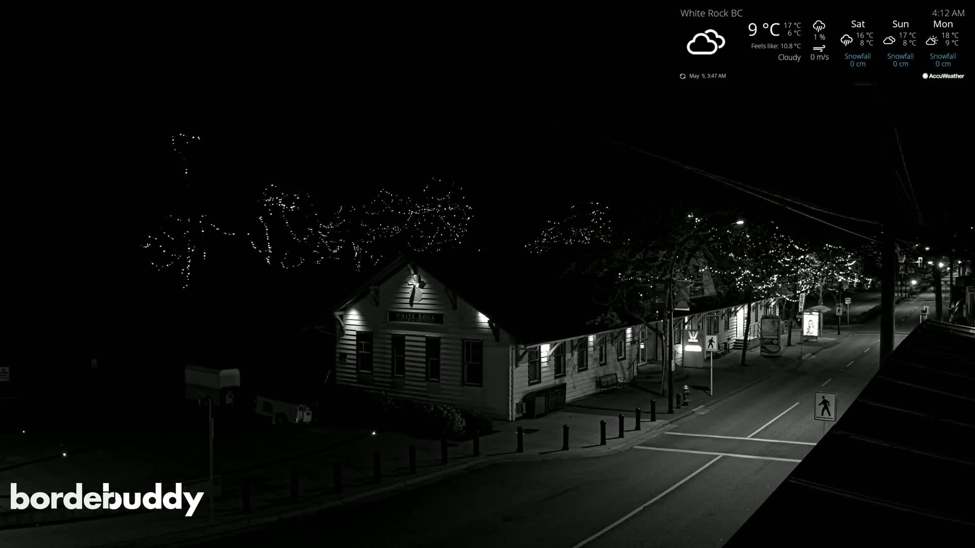 A nighttime, cloudy view of a street scene with a building lit up, featuring trees adorned with string lights.