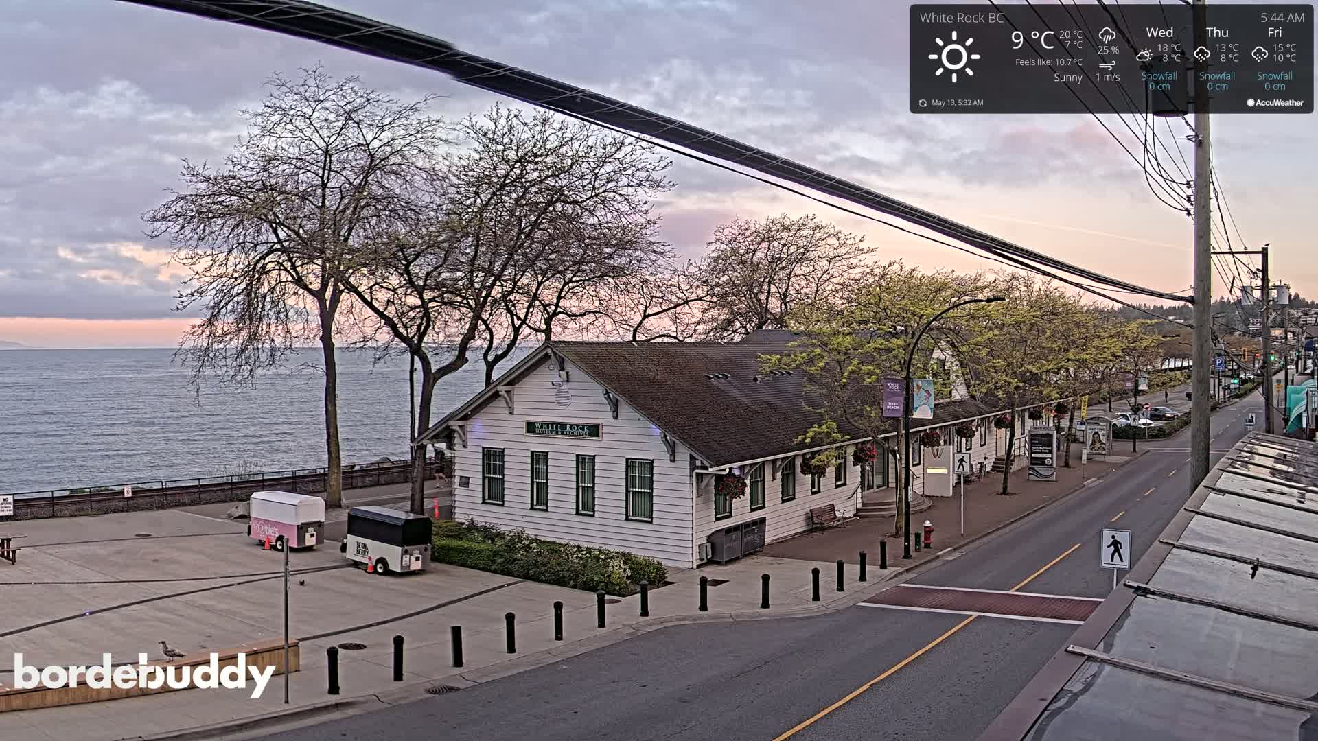 A white building sits near a calm body of water under a partly cloudy, sunrise sky.