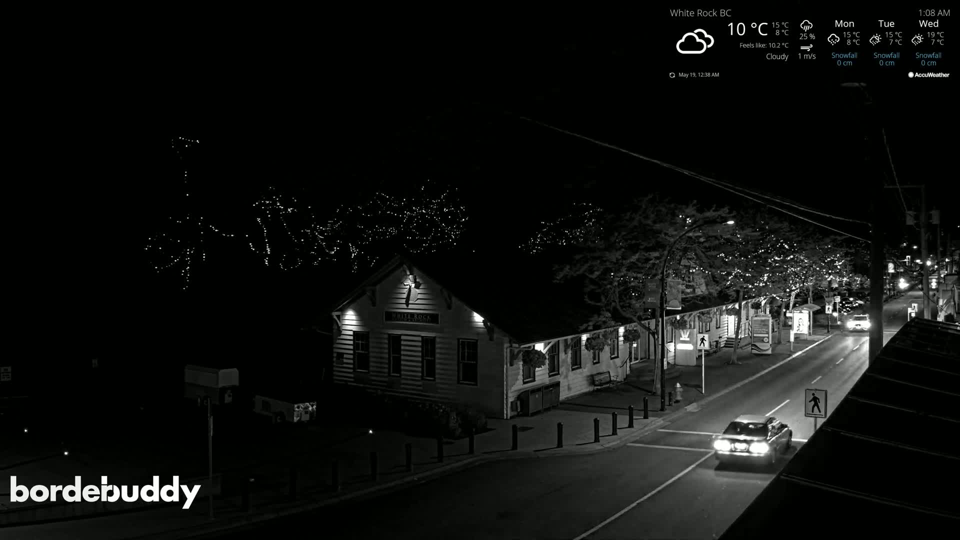 A nighttime, cloudy view of a street scene with a building illuminated, featuring strings of lights in trees.
