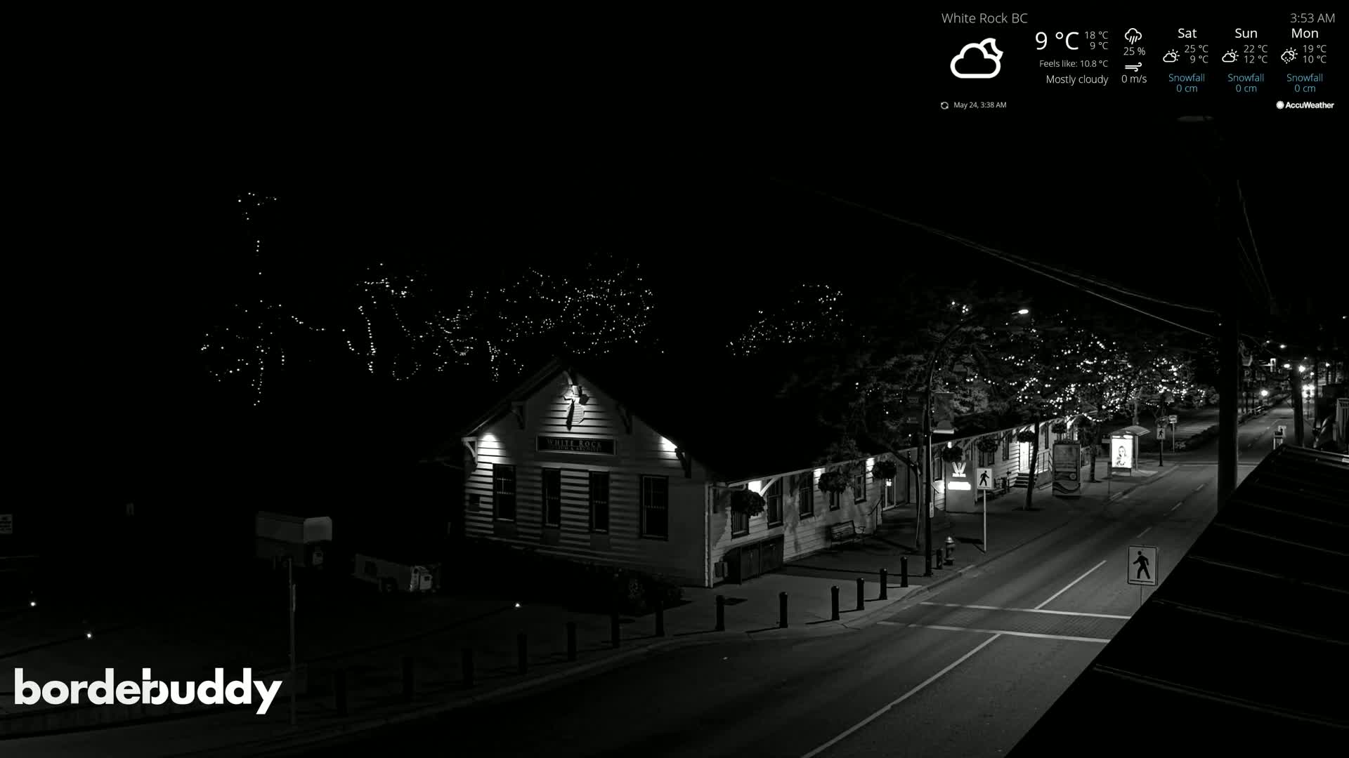 A mostly cloudy night scene shows a street with a building illuminated, string lights in trees, and a mostly empty road.