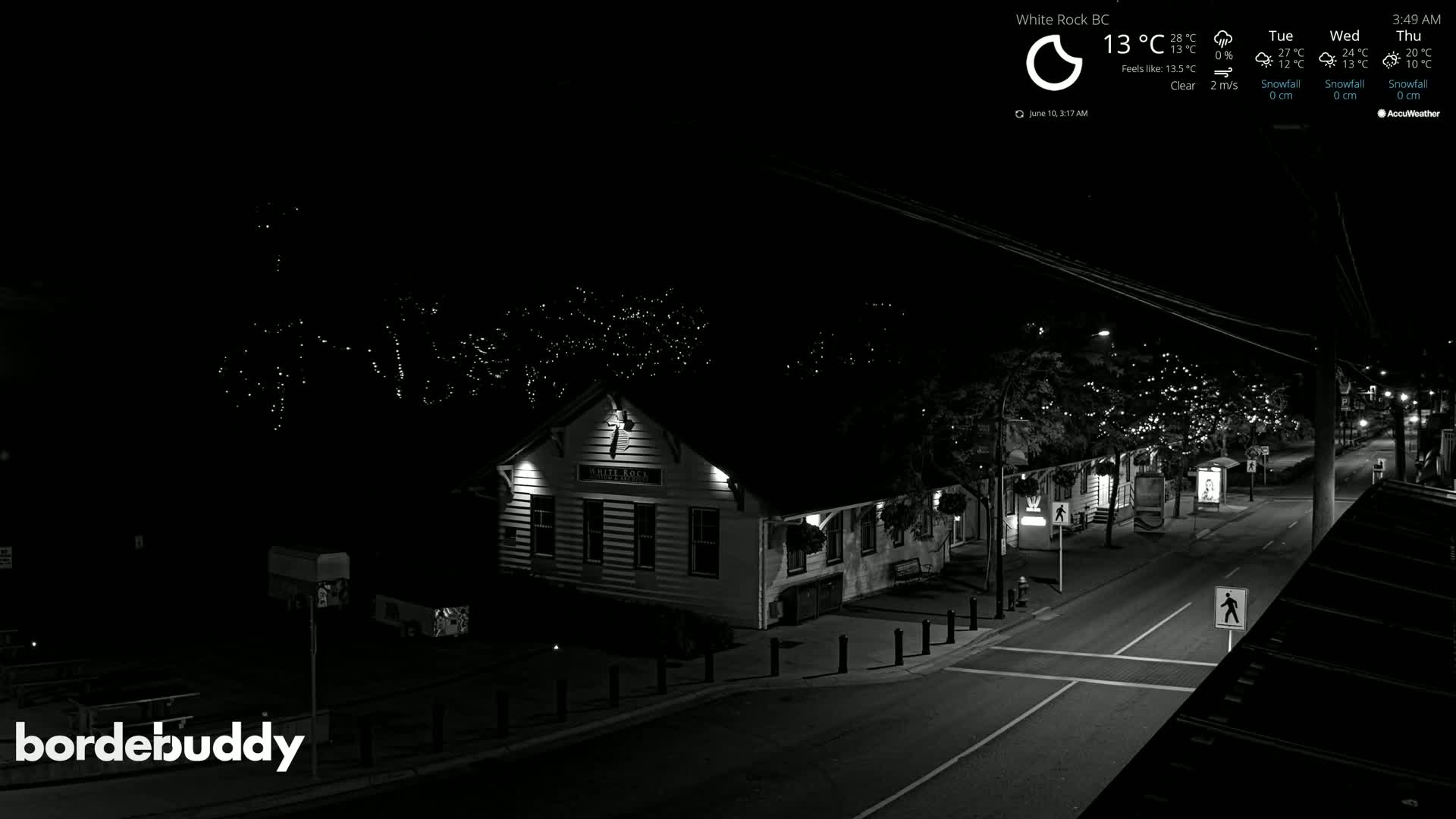 A nighttime, clear-weather view of a street scene featuring a lit building and string lights on trees lining the road.