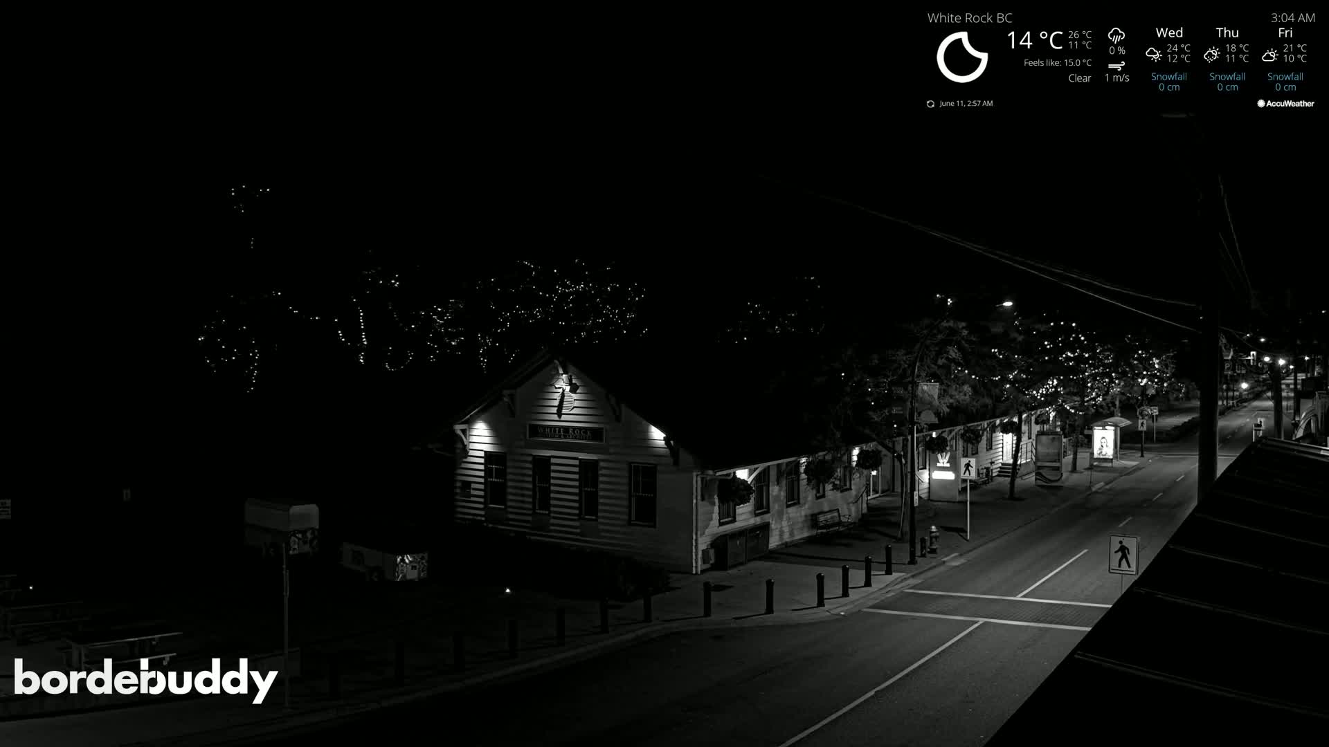 A nighttime, clear-weather view of a street scene shows a building illuminated with string lights on trees along the road.